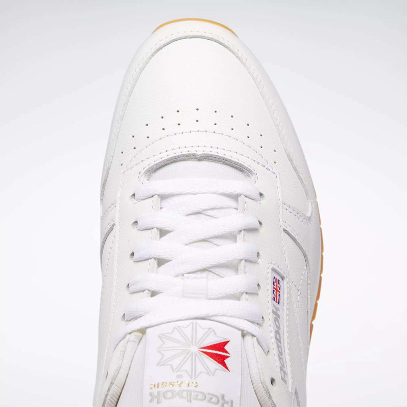Top view of Reebok Classic Leather Shoes featuring white laces, durable leather, perforated toe detailing, a red and grey logo on the tongue, and a small Union Jack flag on the side for retro style.