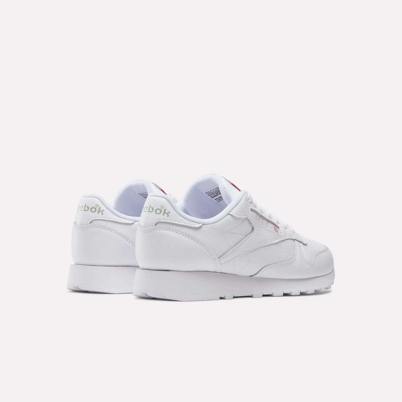 A pair of white Reebok Classic Leather Shoes is displayed on a light background—one shoe faces forward while the other shows the heel and side branding, accentuating these retro-inspired sneakers.