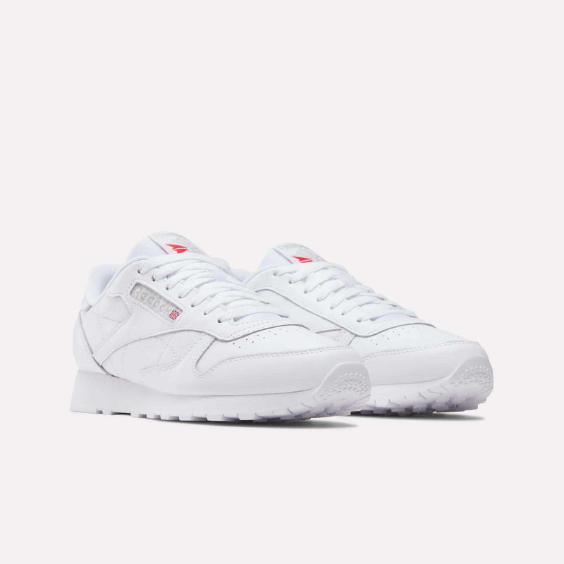 A pair of Reebok Classic Leather Shoes in white with subtle gray accents, low-top design, perforated toe, white laces, and red Reebok logos on the tongue and side, displayed on a plain light background.