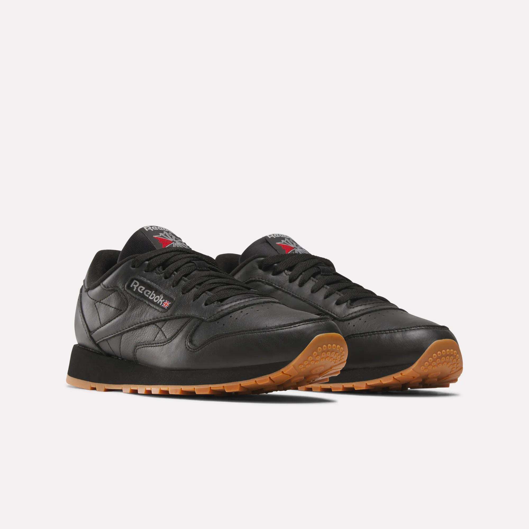 A pair of Reebok Classic Leather Shoes shown on a plain white background, featuring durable black leather uppers, gum rubber soles, the Reebok logo, and a Union Jack flag on the side and tongue.