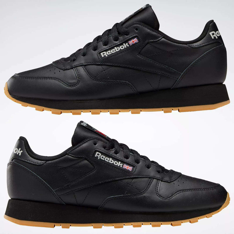 Two black Reebok Classic Leather Shoes with durable leather uppers and tan rubber soles, shown from the side. The Reebok logo and Union Jack are displayed near the laces.