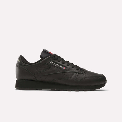 A side-profile view shows the Reebok Classic Leather Shoes in black with a durable leather upper, black laces and sole, plus the Reebok logo and Union Jack flag on the side, set against a white background.