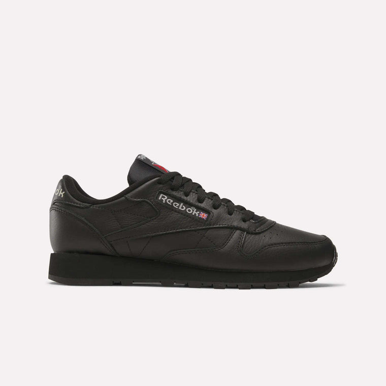 Reebok Classic Leather Shoes in black feature a durable leather upper, signature logo and UK flag on the side, black laces, and a rubber sole—retro-inspired sneakers ideal for any look, showcased in side profile on a white background.