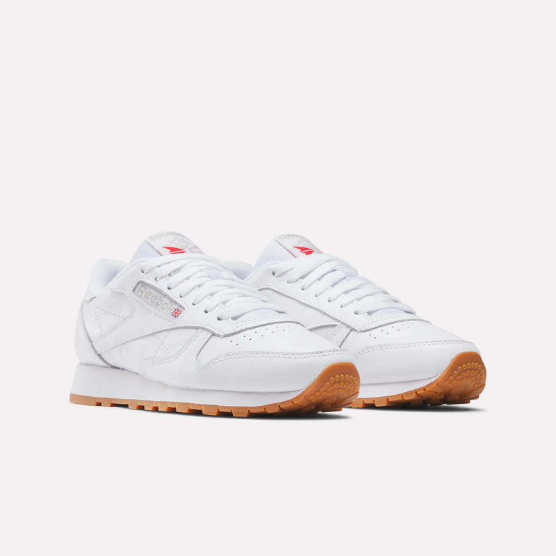 A pair of Reebok Women's Classic Leather Shoes in white with gum rubber soles, cushioned midsoles, and red logos on the tongue and side, shown on a plain white background.
