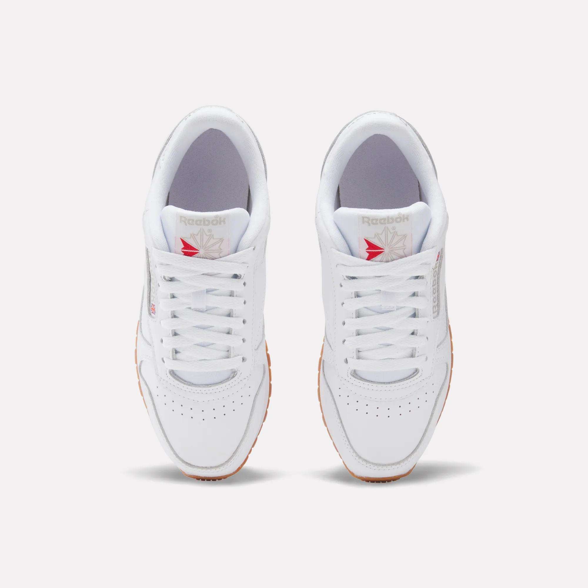 Top view of Reebok Women's Classic Leather Shoes in white with gum soles, red and gray Reebok logo, cushioned midsole, shown side by side on a plain light background.
