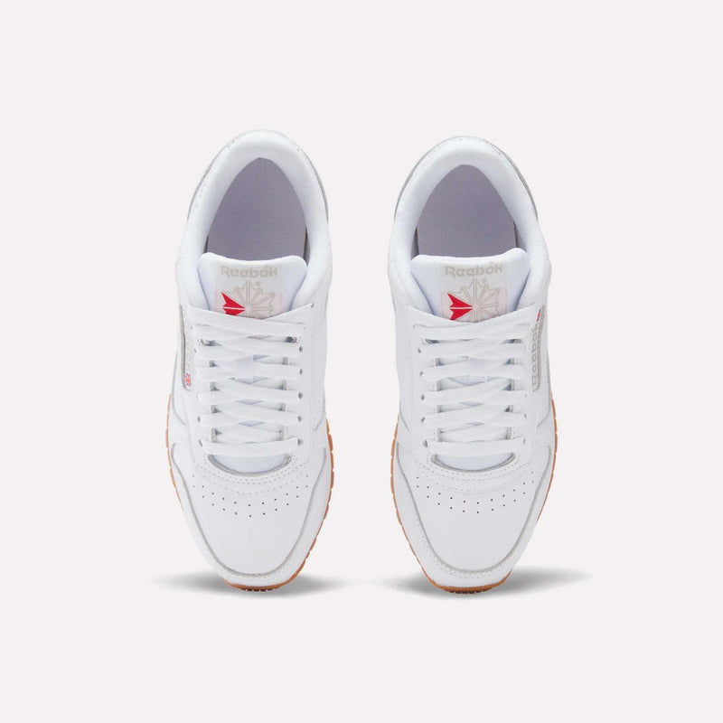 A top view of Women's Classic Leather Shoes by Reebok in white, with gum soles, perforated toe box, cushioned midsole, and red and grey Reebok logos on the tongue and side.