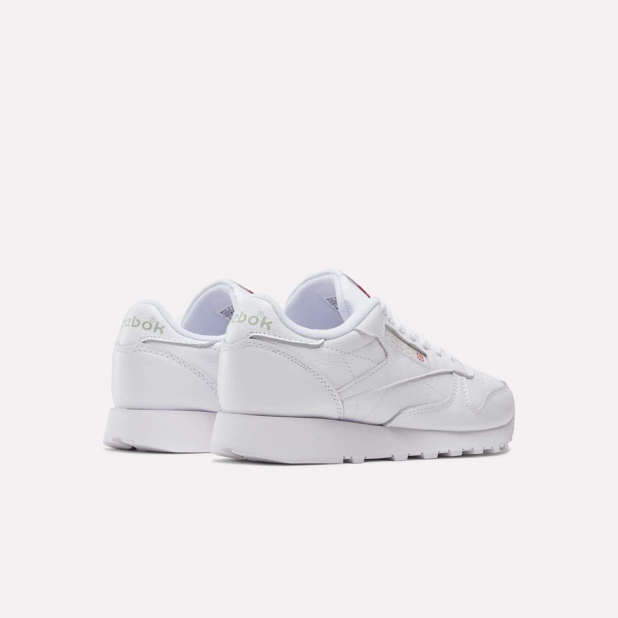 A pair of Reebok Women's Classic Leather Shoes are angled from the back, showcasing the Reebok logo on the heel and side, plus a cushioned midsole for comfort, set against a plain light background.