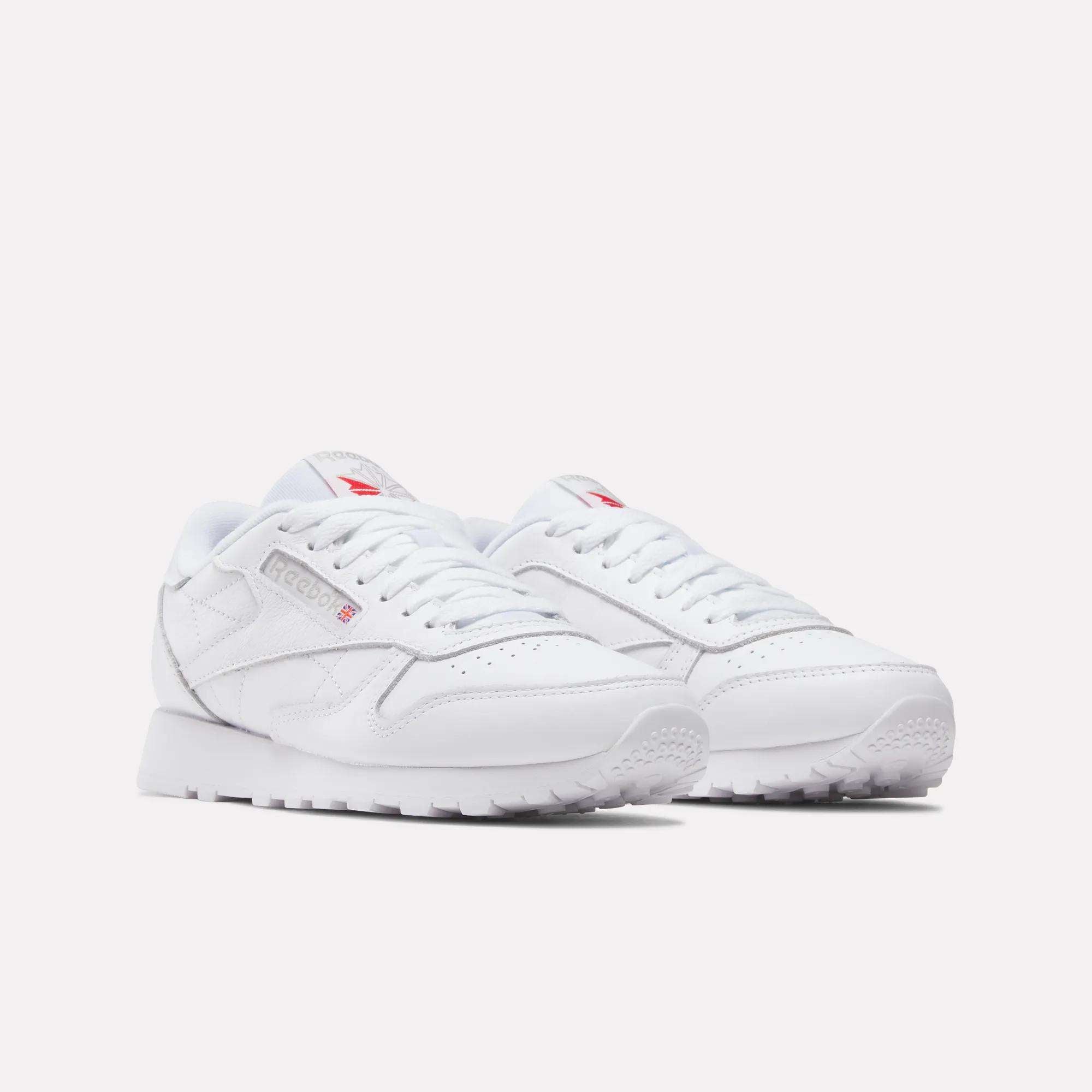 A pair of Women's Classic Leather Shoes by Reebok, featuring cushioned midsoles, white laces and soles, with subtle grey and red logo accents, displayed on a light background.