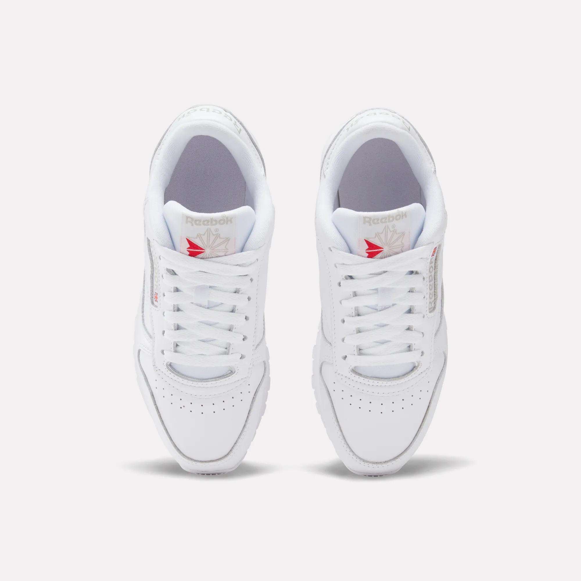 Top view of Reebok Women's Classic Leather Shoes, white leather with cushioned midsole and red star logo on the tongue, shown side by side on a plain white background.