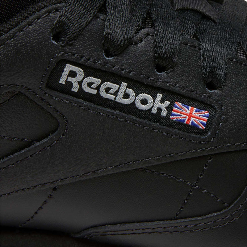 Close-up of Women's Classic Leather Shoes by Reebok, featuring black leather, black laces, stitched details, the Reebok logo, and a small Union Jack flag—an iconic women's footwear choice.