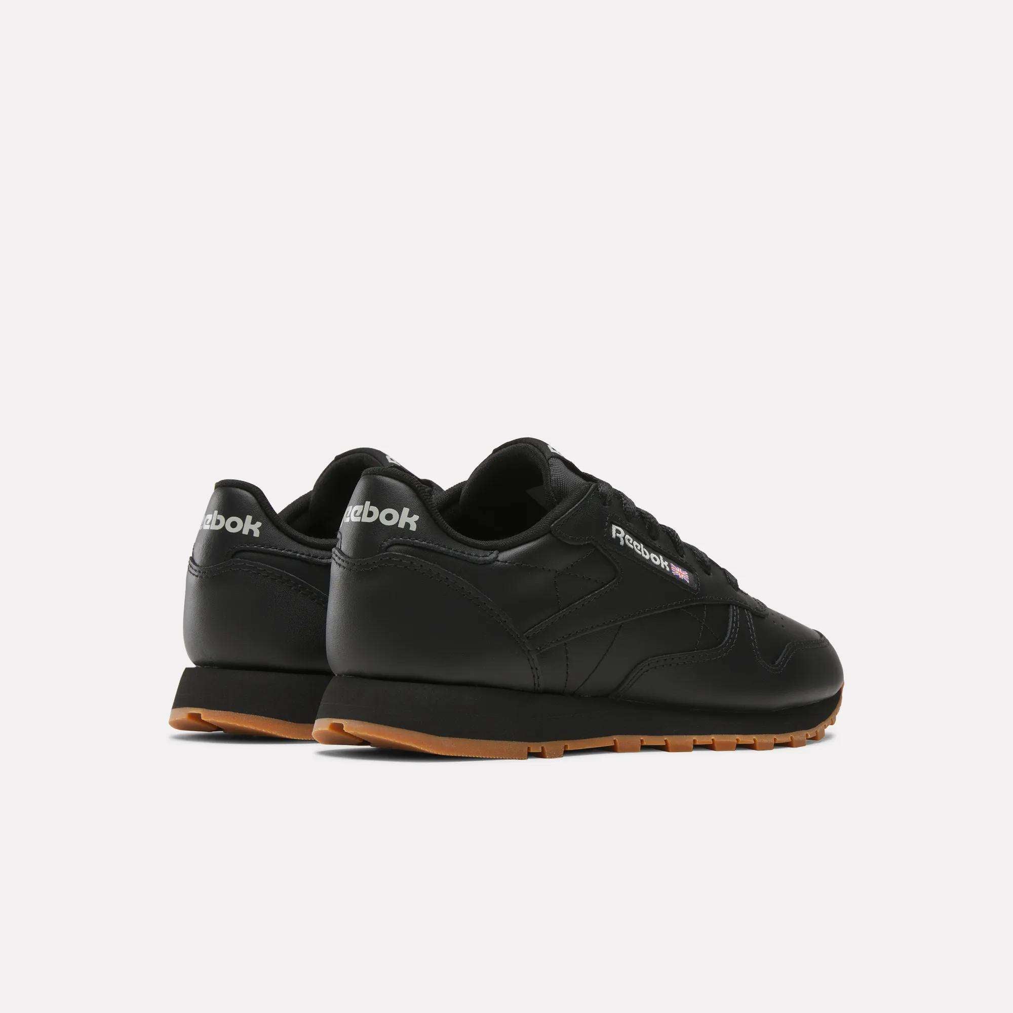 A pair of Reebok Women's Classic Leather Shoes in black with gum soles and a cushioned midsole, shown from the back and side on a plain white background.
