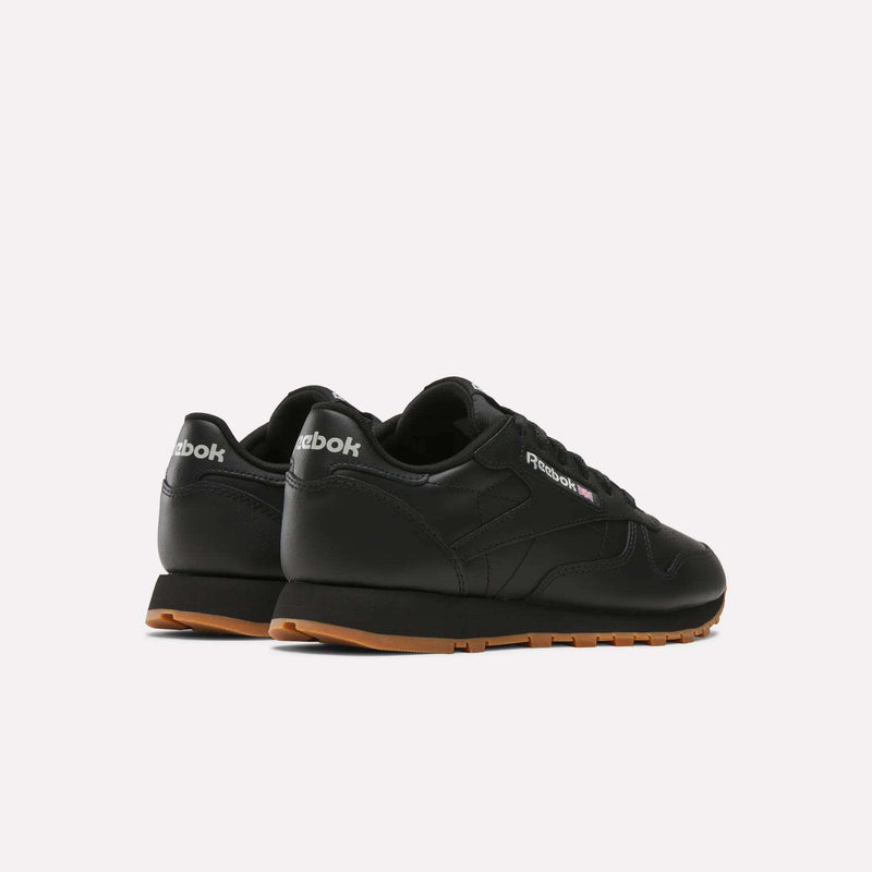 A pair of Reebok Women's Classic Leather Shoes in black with gum soles and a cushioned midsole, shown from the back and side on a plain white background.