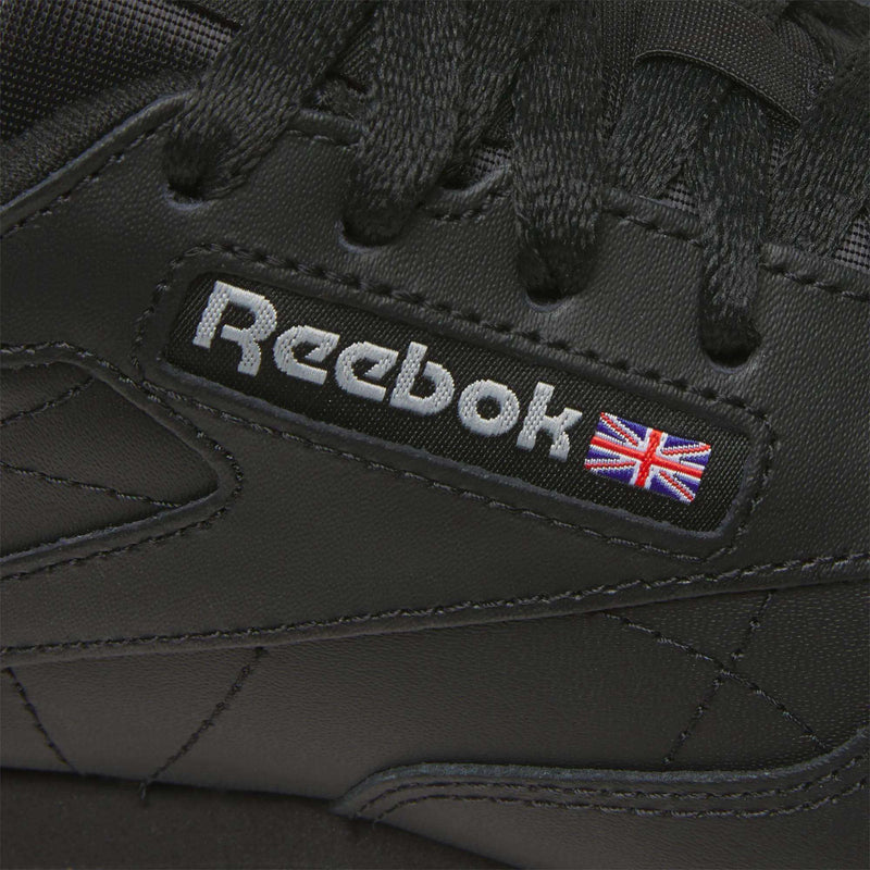 Close-up of Reebok Women's Classic Leather Shoes in black, showcasing the Reebok logo, a small Union Jack flag by the laces, and a cushioned midsole for comfort.