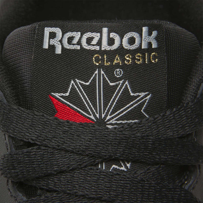 Close-up of a Women's Reebok Classic Leather Shoe tongue, showing the white Reebok logo and CLASSIC in gold above a stylized maple leaf, with black laces in front and a cushioned midsole for comfort.