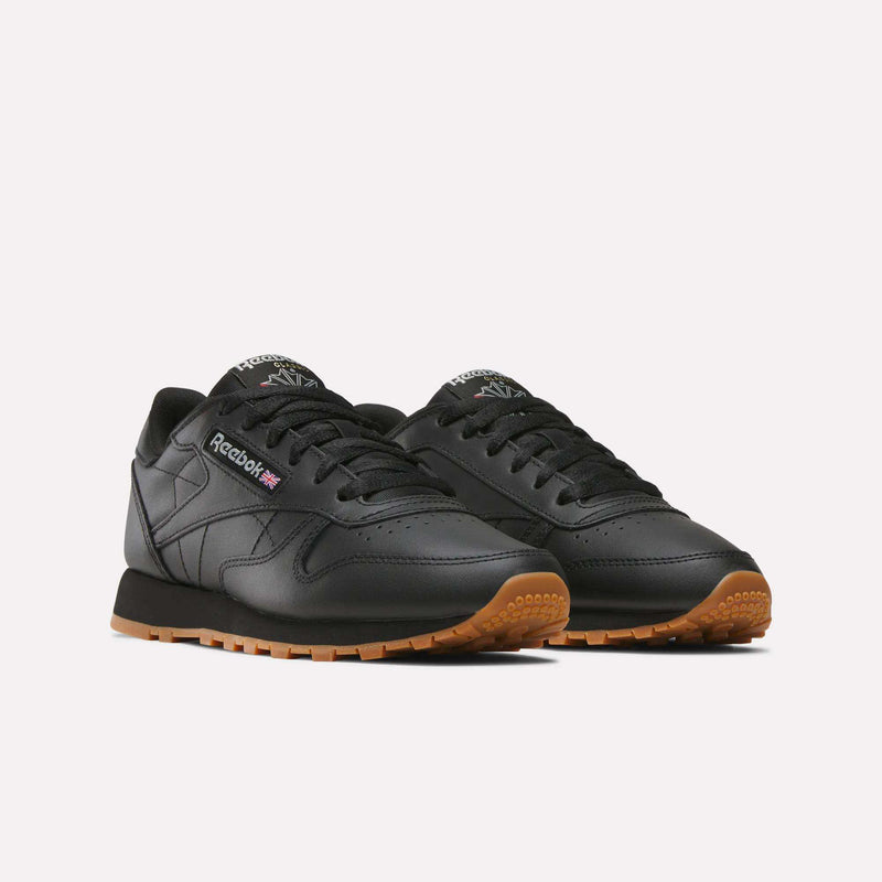 A pair of Reebok Women's Classic Leather Shoes in black, featuring gum rubber soles, cushioned midsoles, black laces, and the Reebok logo on the side, displayed against a plain white background.