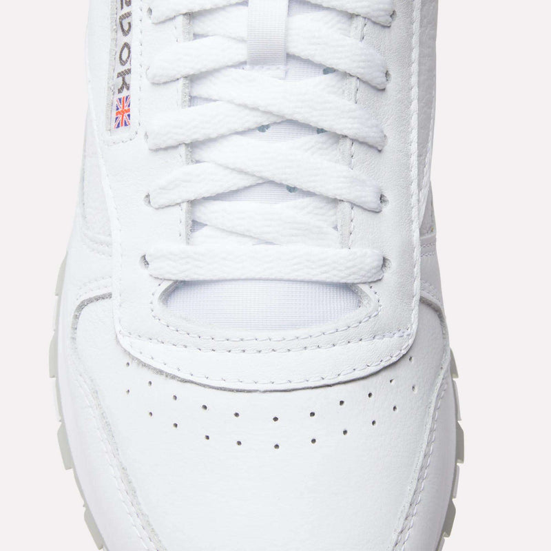 Close-up of Reebok Classic Leather Shoes with laces, a perforated toe box, textured leather, and a small Union Jack flag detail by the eyelets—iconic elements from Reebok’s retro design.