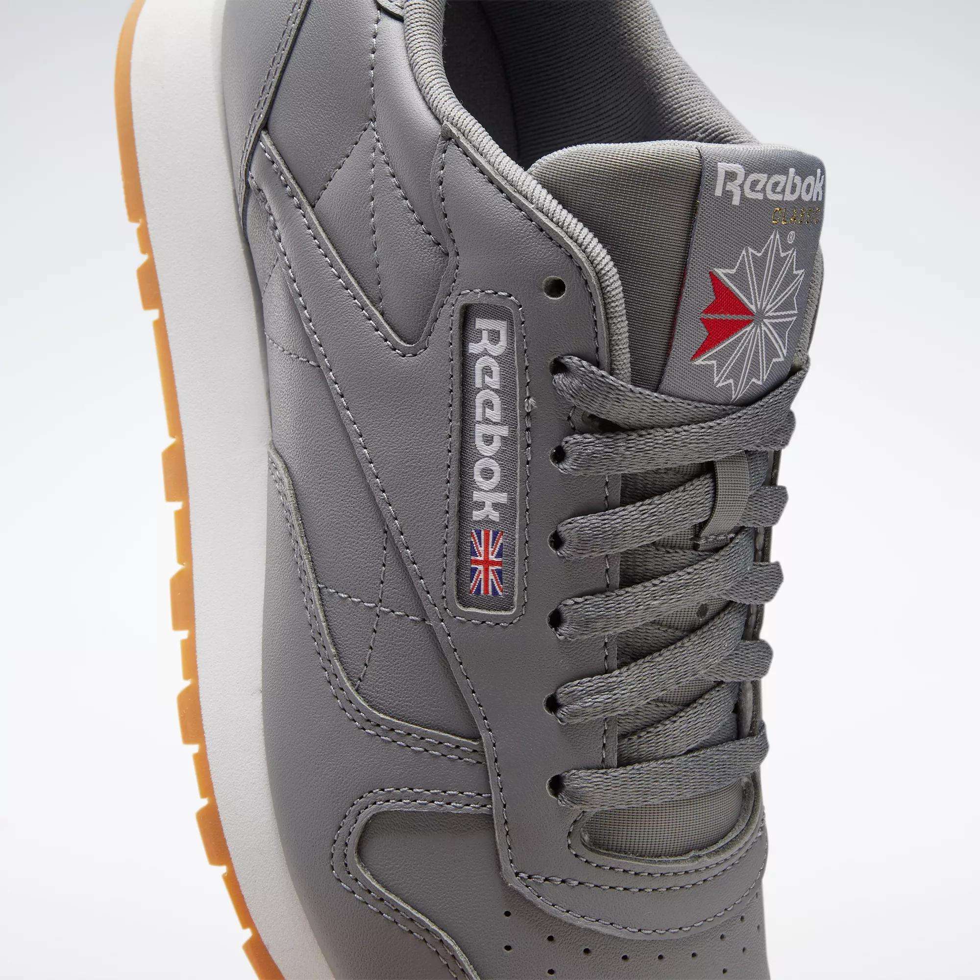 A close-up of Reebok’s Classic Leather Shoes in gray, featuring a gum sole, side Reebok logo with Union Jack flag, quilted stitching, durable leather upper, and gray laces—ideal for lovers of retro style.