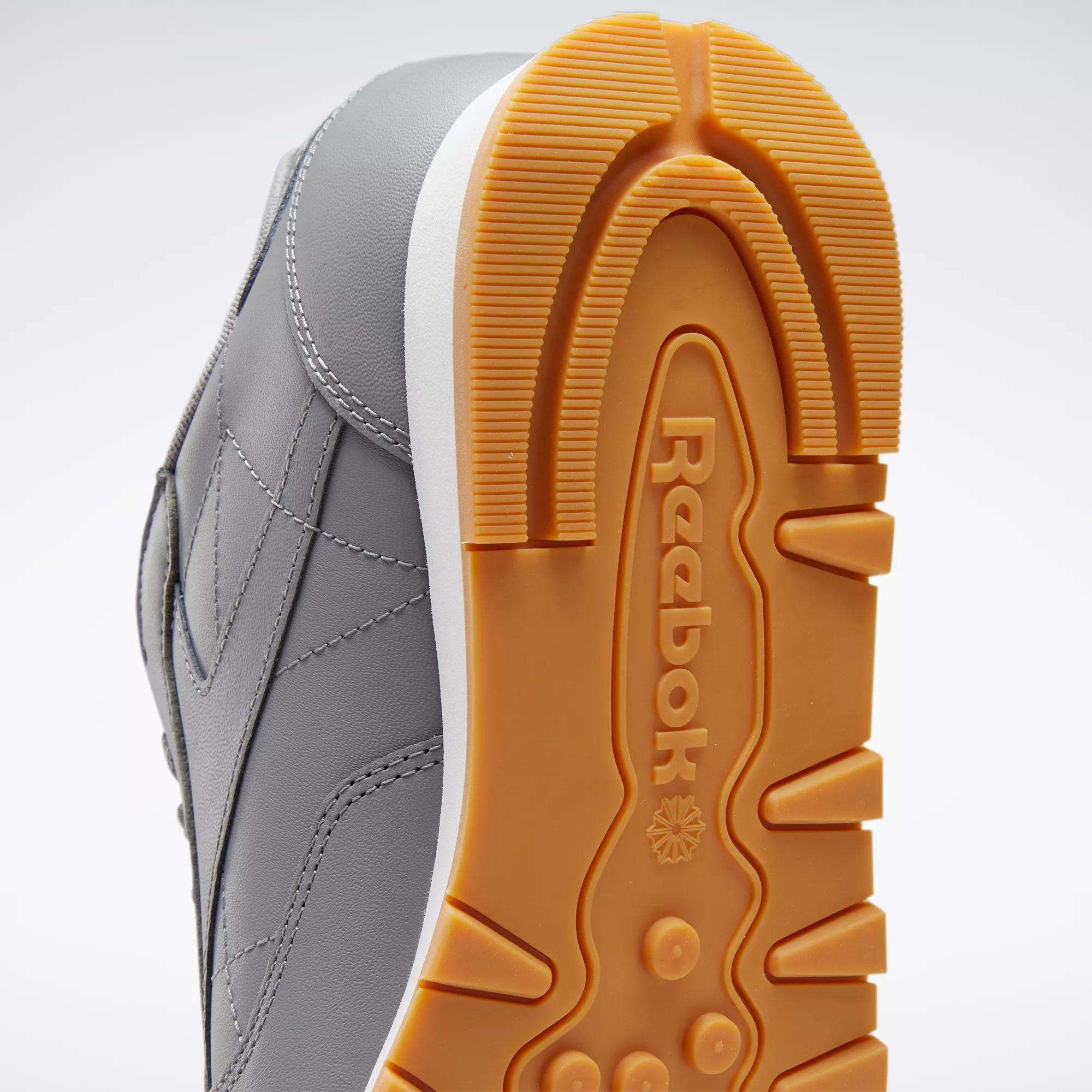 A close-up of Reebok Classic Leather Shoes highlights the durable leather upper, orange and white sole, visible Reebok logo, and textured grip pattern.