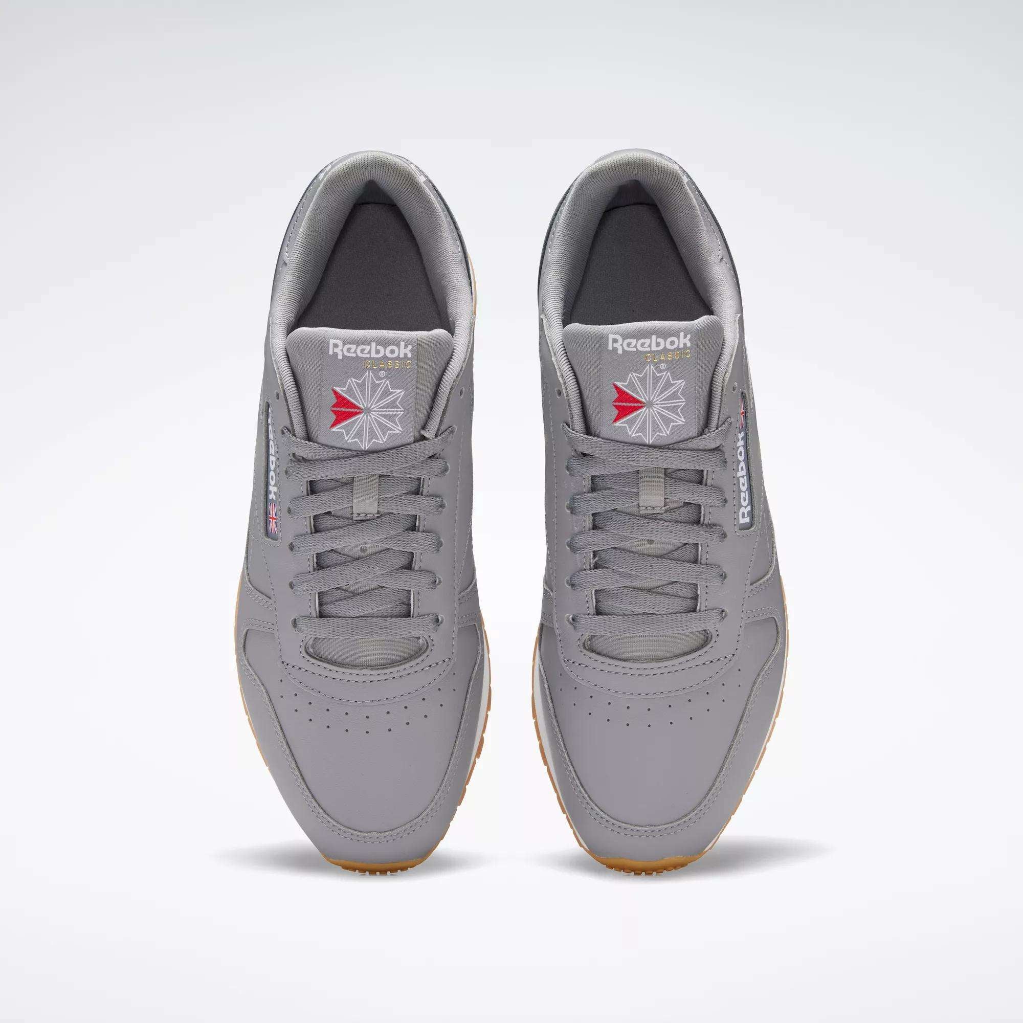 A pair of gray Reebok Classic Leather Shoes viewed from above, showcasing a durable leather upper, laces, perforated toes, and the Reebok logo with a red and gray emblem on the tongue and side.