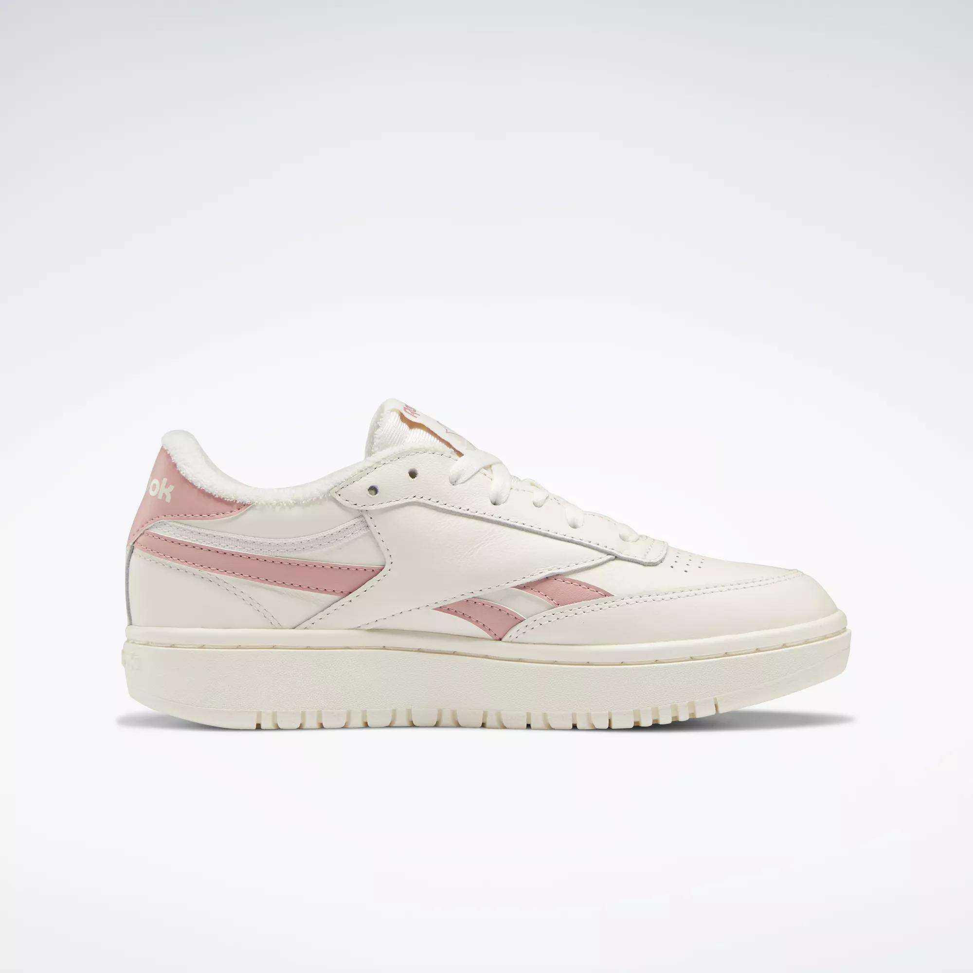 The Reebok Women's Club C Double Revenge Shoes are low-top white sneakers with light pink accents on the side stripe, heel, and tongue, featuring a leather upper. Shown in a side view against a plain white background.