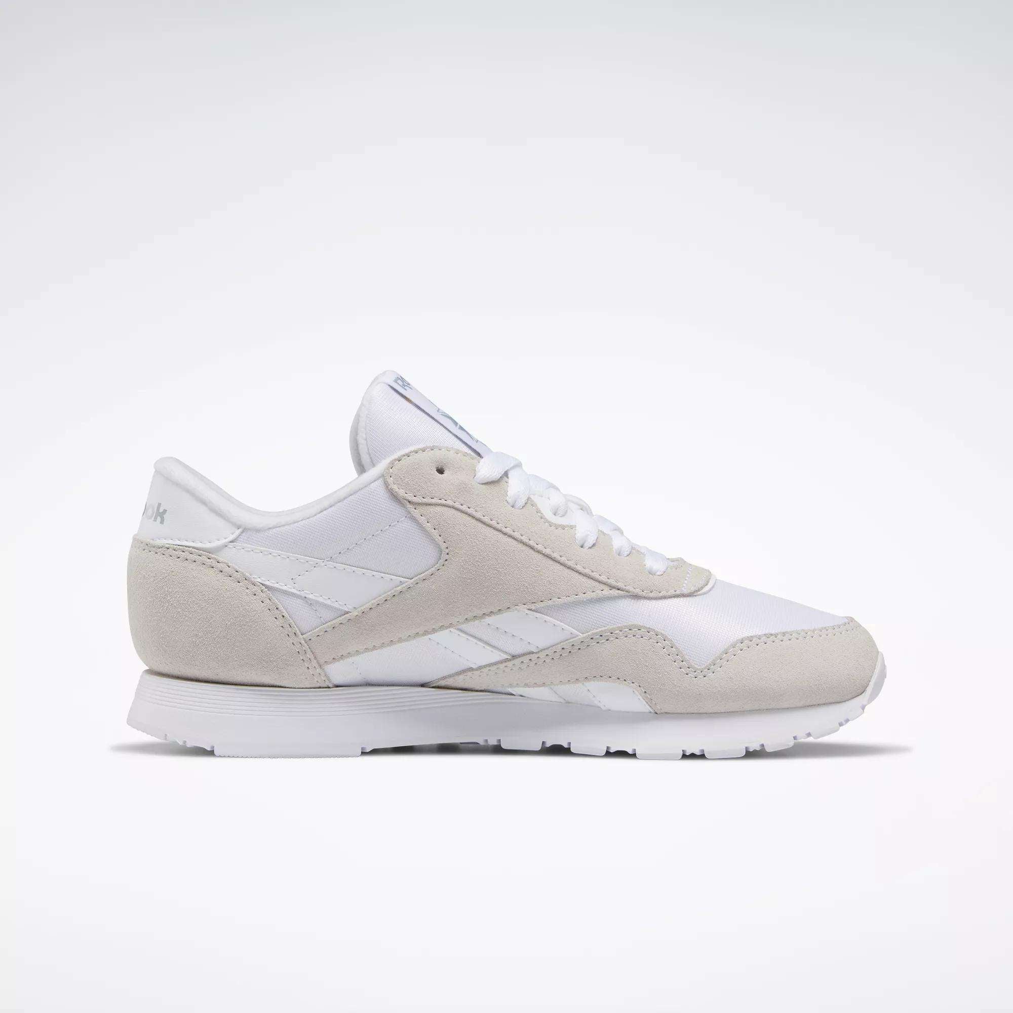 The Women's Classic Nylon Shoes by Reebok feature a white and light gray design with suede and mesh details, white laces, a flat rubber sole, and a low profile—shown from the side against a plain white background.