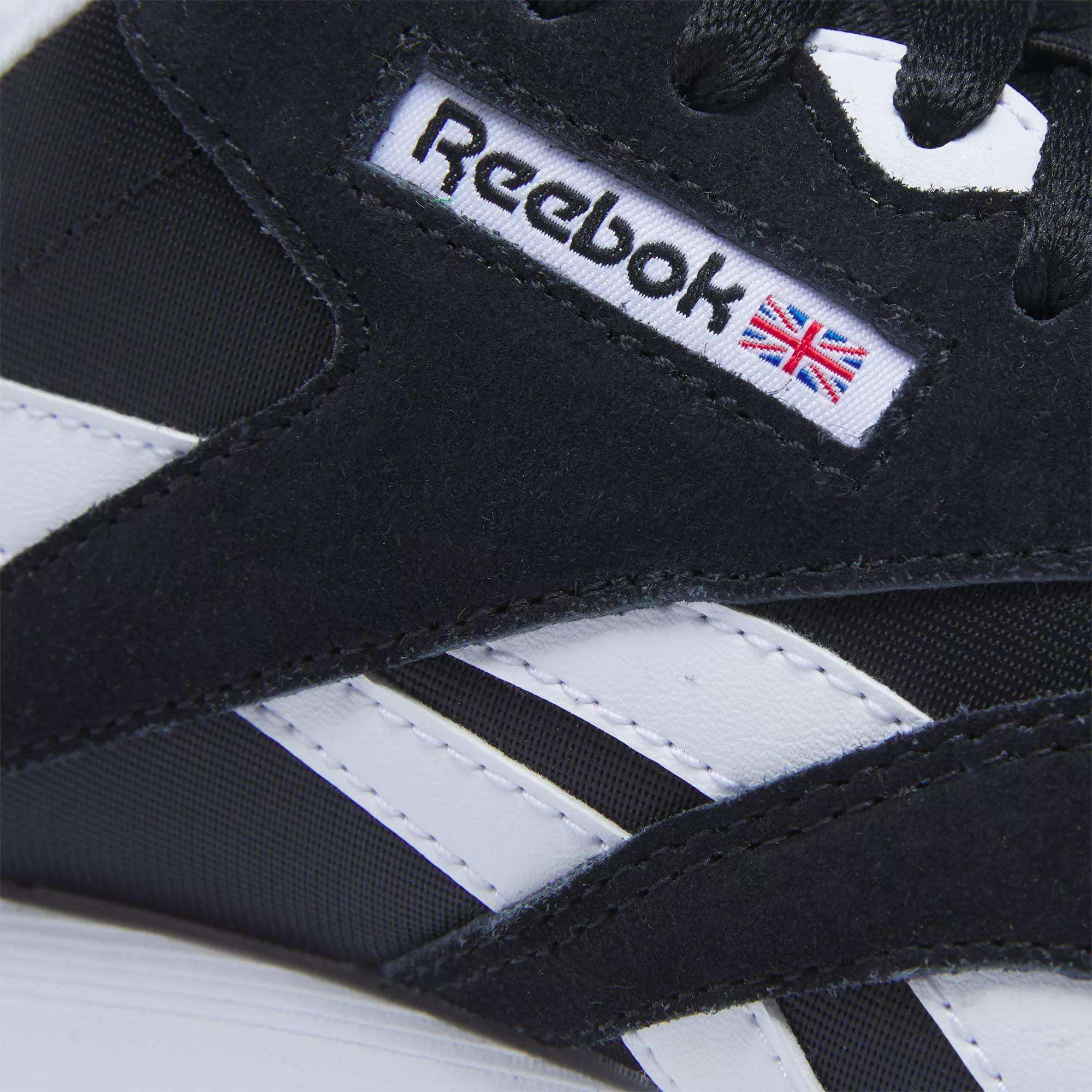 Close-up of Reebok Women's Classic Nylon Shoes in black and white, showcasing suede details, the iconic Reebok logo, a small British flag on the side, and visible stitching and texture.