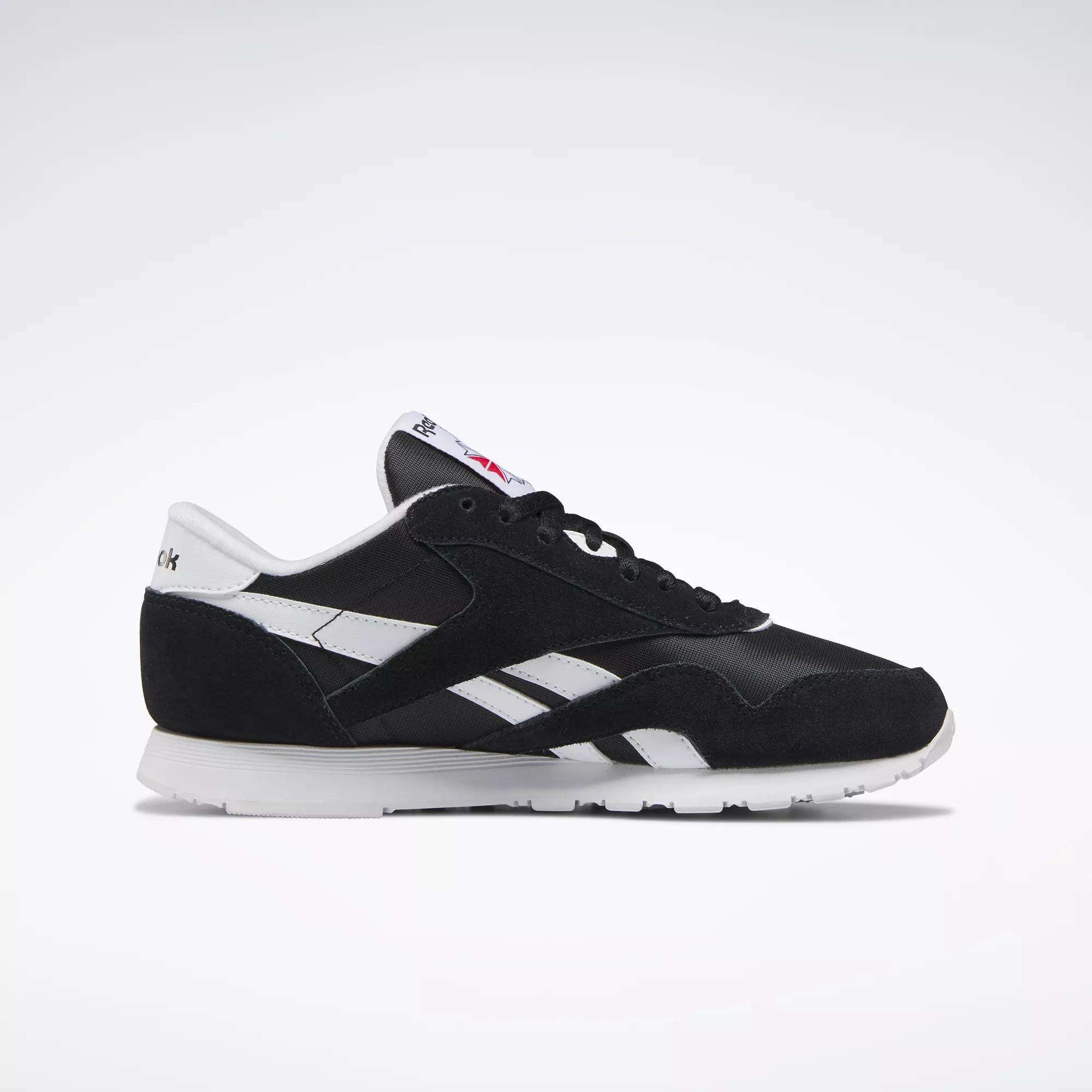 The Reebok Women's Classic Nylon Shoes feature a black upper, white side stripes, suede accents, and a white sole with logo details—shown in side profile on a light background. Stylish and comfortable sneakers for everyday wear.