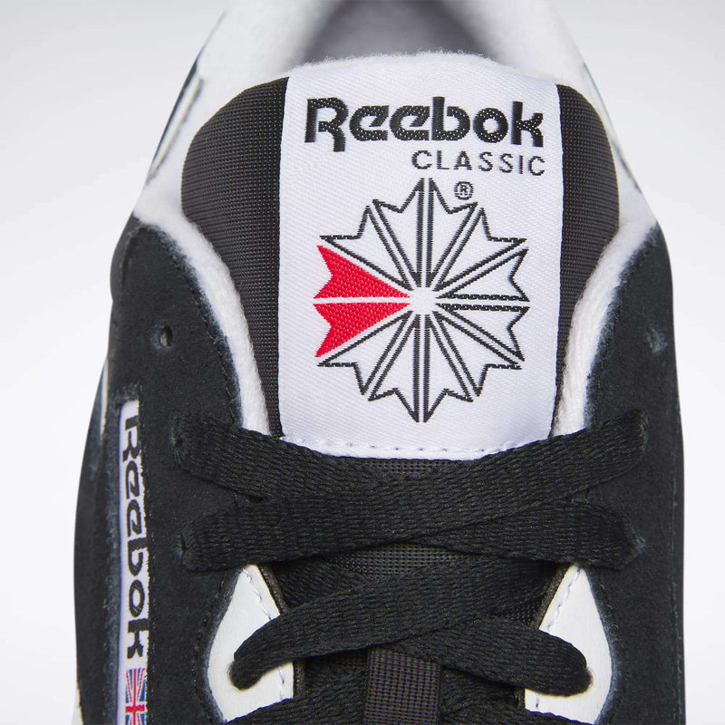 Close-up of the tongue of a black Reebok Men's Classic Nylon Shoe, highlighting the Reebok logo, red and grey starburst, black laces, and a small Union Jack flag—signature details of these classic sneakers.