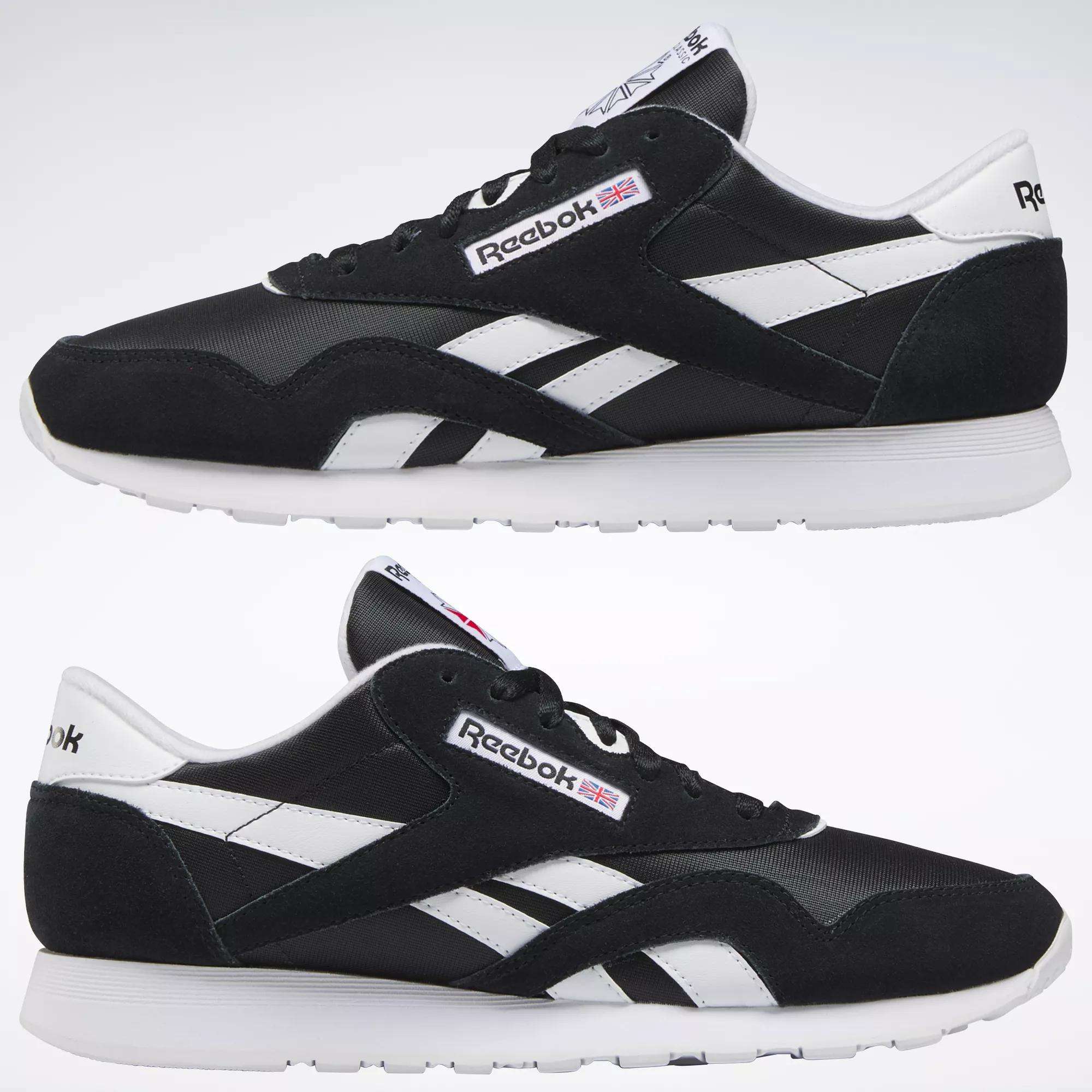 Two black Reebok Men's Classic Nylon Shoes with white soles and side stripes are shown side by side on a plain background. The Reebok logo and a small UK flag appear on the sides and tongue of these classic sneakers.