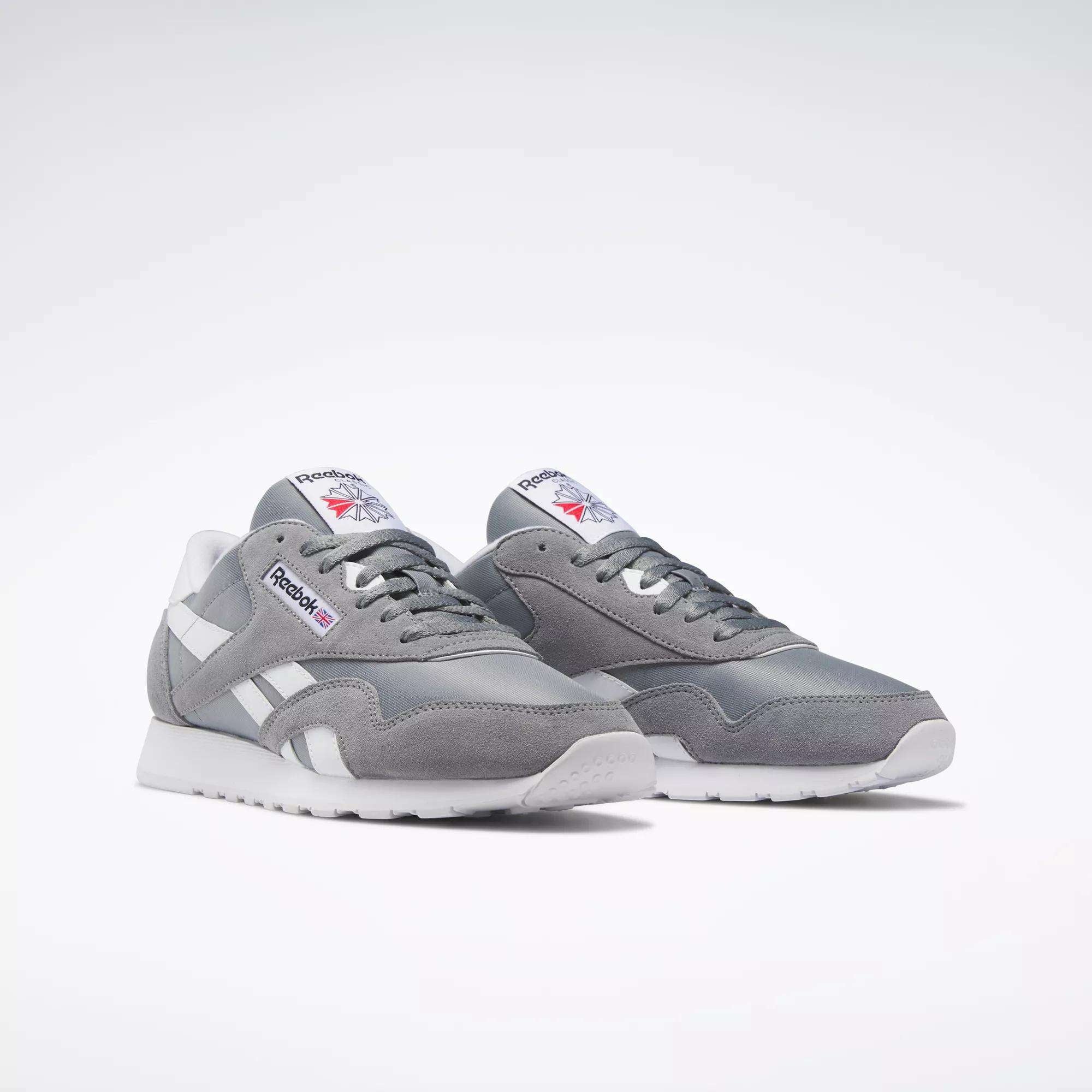 The Reebok Men's Classic Nylon Shoes are light gray everyday sneakers with white accents and laces, a durable nylon upper, and the Reebok logo on the side and tongue, shown against a plain white background.