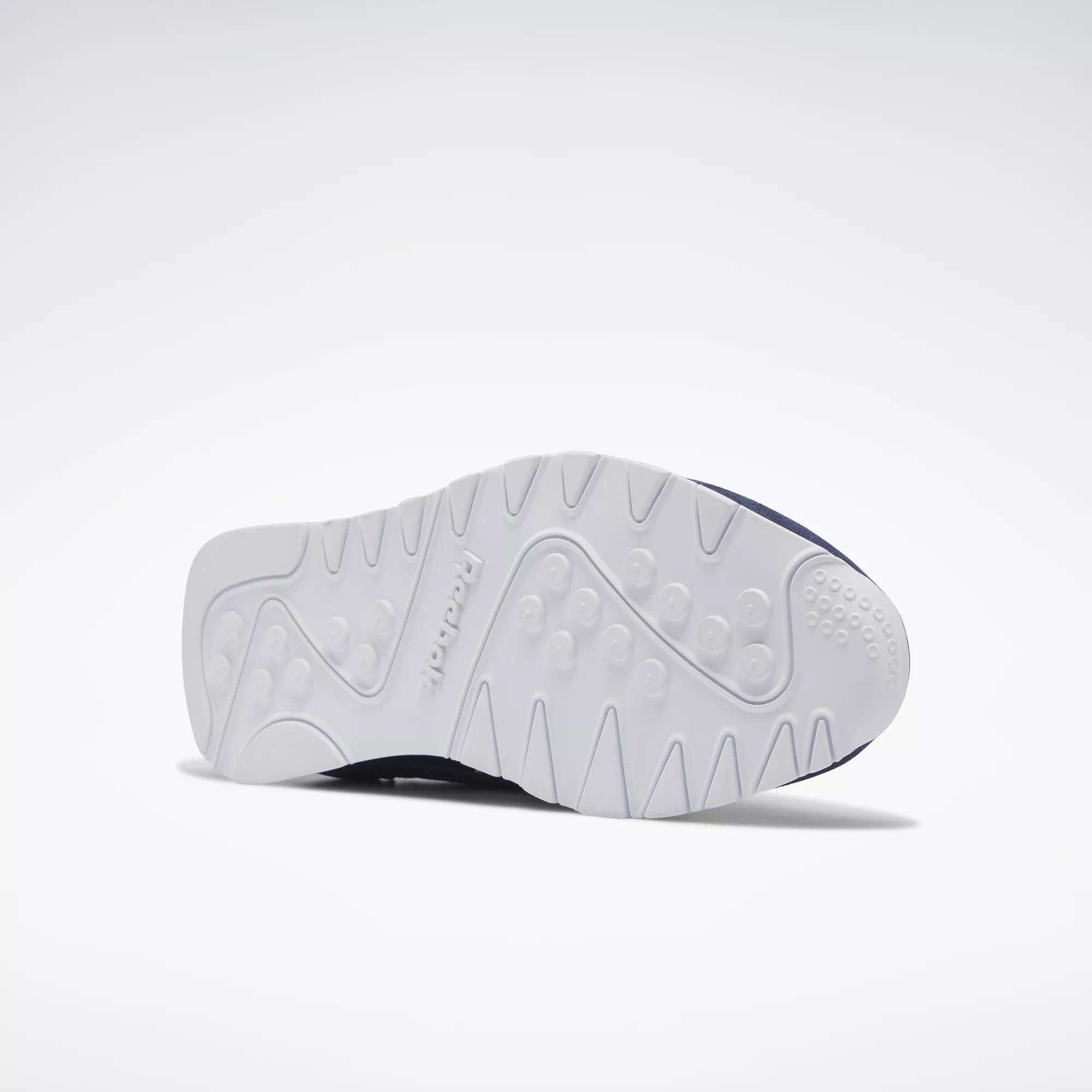 The Reebok Men's Classic Nylon Shoes are shown on their side against a plain light background, displaying the white textured sole with tread patterns and Reebok branding, emphasizing the grip of these classic everyday sneakers.
