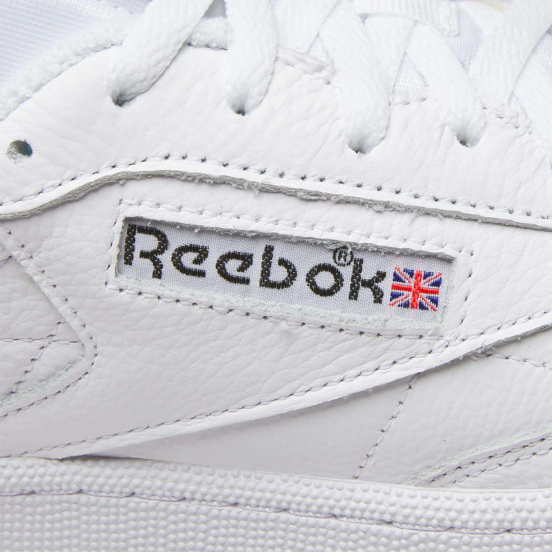 Close-up of Reebok Men's Club C 85 Shoes, featuring the stitched logo and Union Jack flag on the side, with visible leather texture and white laces.