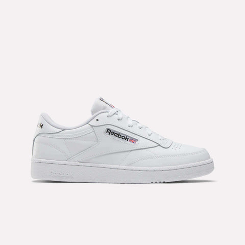 The Reebok Men's Club C 85 Shoes are white low-top sneakers featuring the Reebok logo and a small Union Jack flag on the side, with white laces, detailed stitching, and a textured sole.