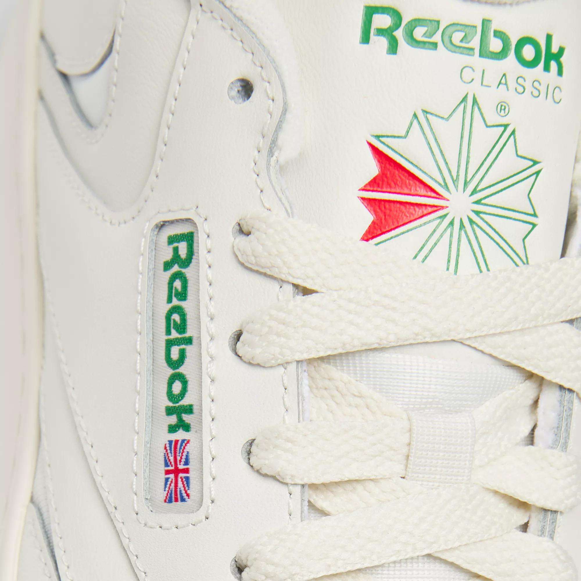 Close-up of Reebok Women's Club C Extra Shoes in white, highlighting the green Reebok logo, red and green star emblem, white laces, an embroidered Union Jack flag, and a modern platform midsole designed for women.
