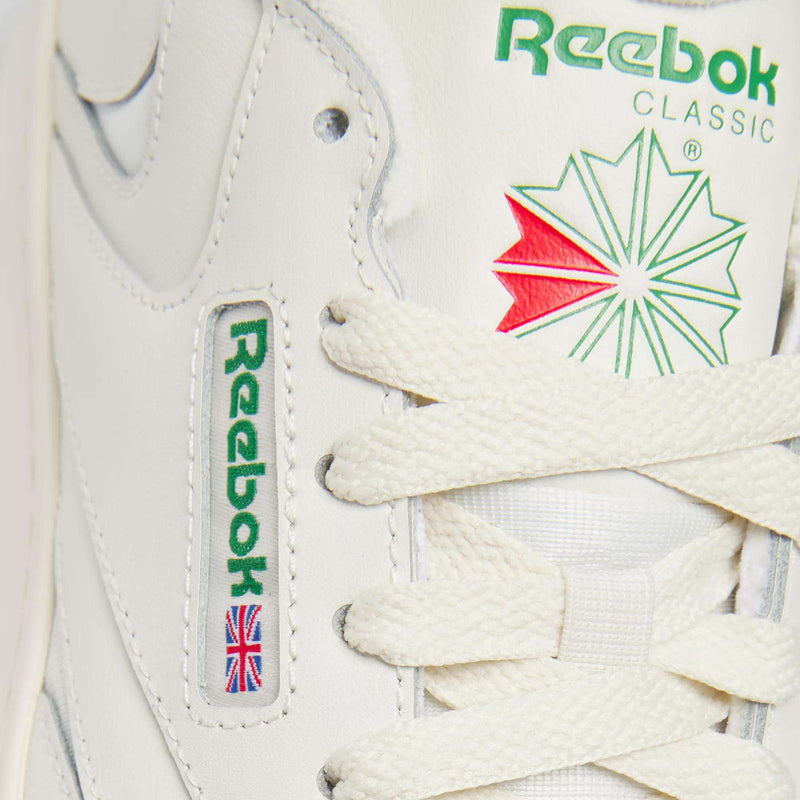 Close-up of Reebok Women's Club C Extra Shoes in white, highlighting the green Reebok logo, red and green star emblem, white laces, an embroidered Union Jack flag, and a modern platform midsole designed for women.