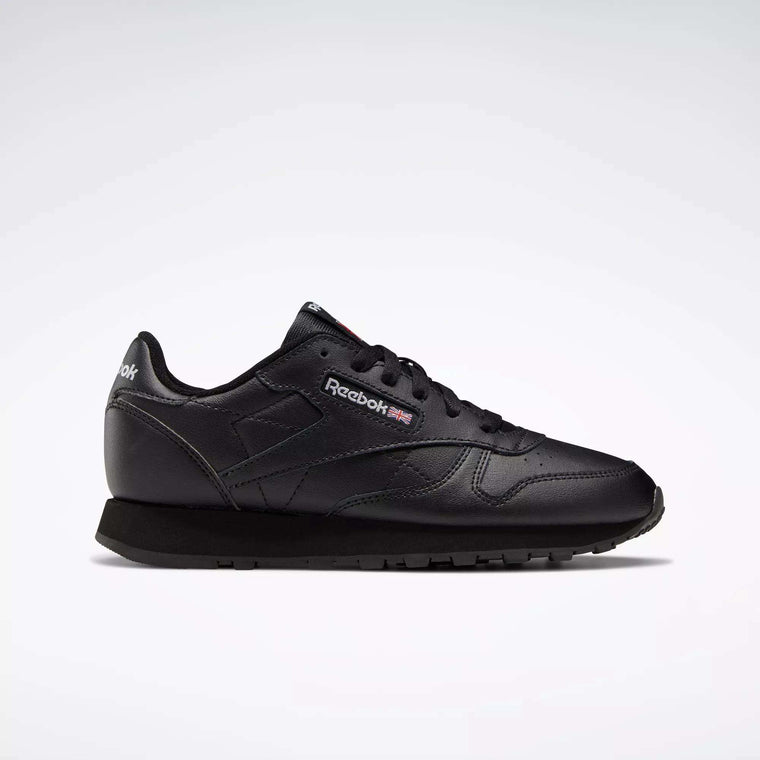 The Reebok Classic Leather Shoes - Big Kids feature an all-black design with matching laces and sole, subtle Reebok branding on the side, and are displayed against a plain light background for a timeless look.