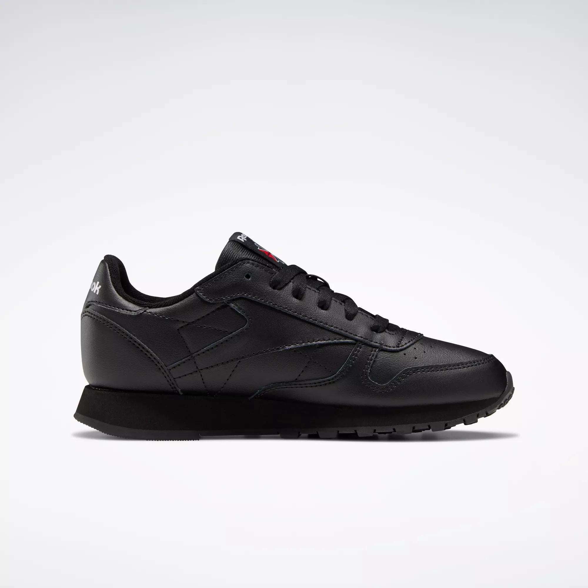 The Reebok Classic Leather Shoes - Big Kids feature a black low-top design with matching laces and sole, displayed in profile on a light gray background—ideal for those seeking timeless boys’ footwear.