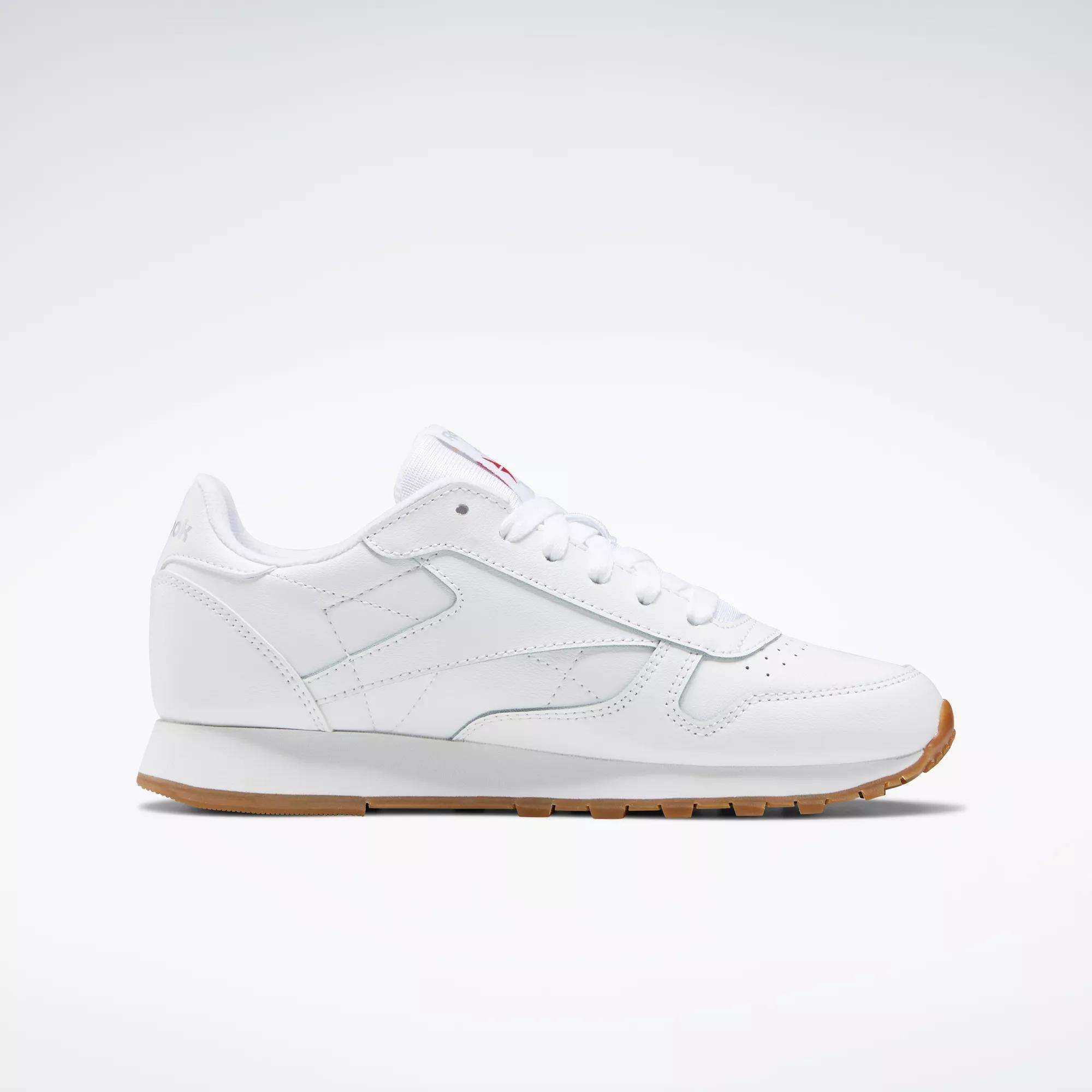 The Reebok Classic Leather Shoes - Big Kids feature a white leather upper, classic stitched side-stripe, white laces and sole, plus a light brown rubber outsole. Shown in side profile against a plain background. Ideal for junior boys' shoe collections.