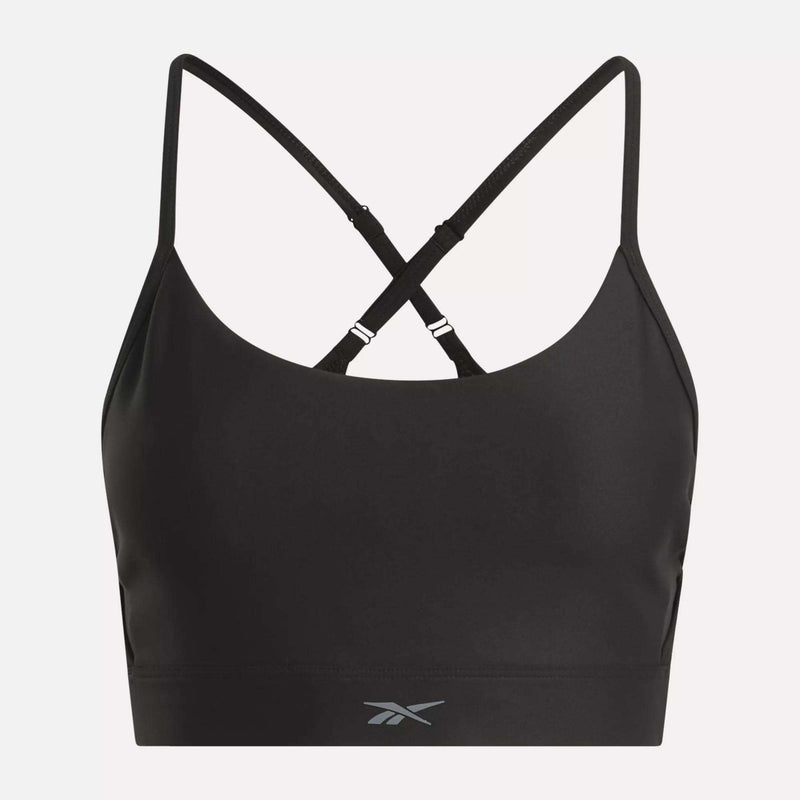The Reebok Women's Lux Strappy Sports Bra is black with sweat-wicking fabric, thin adjustable crisscross straps, and a gray Reebok logo on the front bottom band. The product is shown against a plain white background.