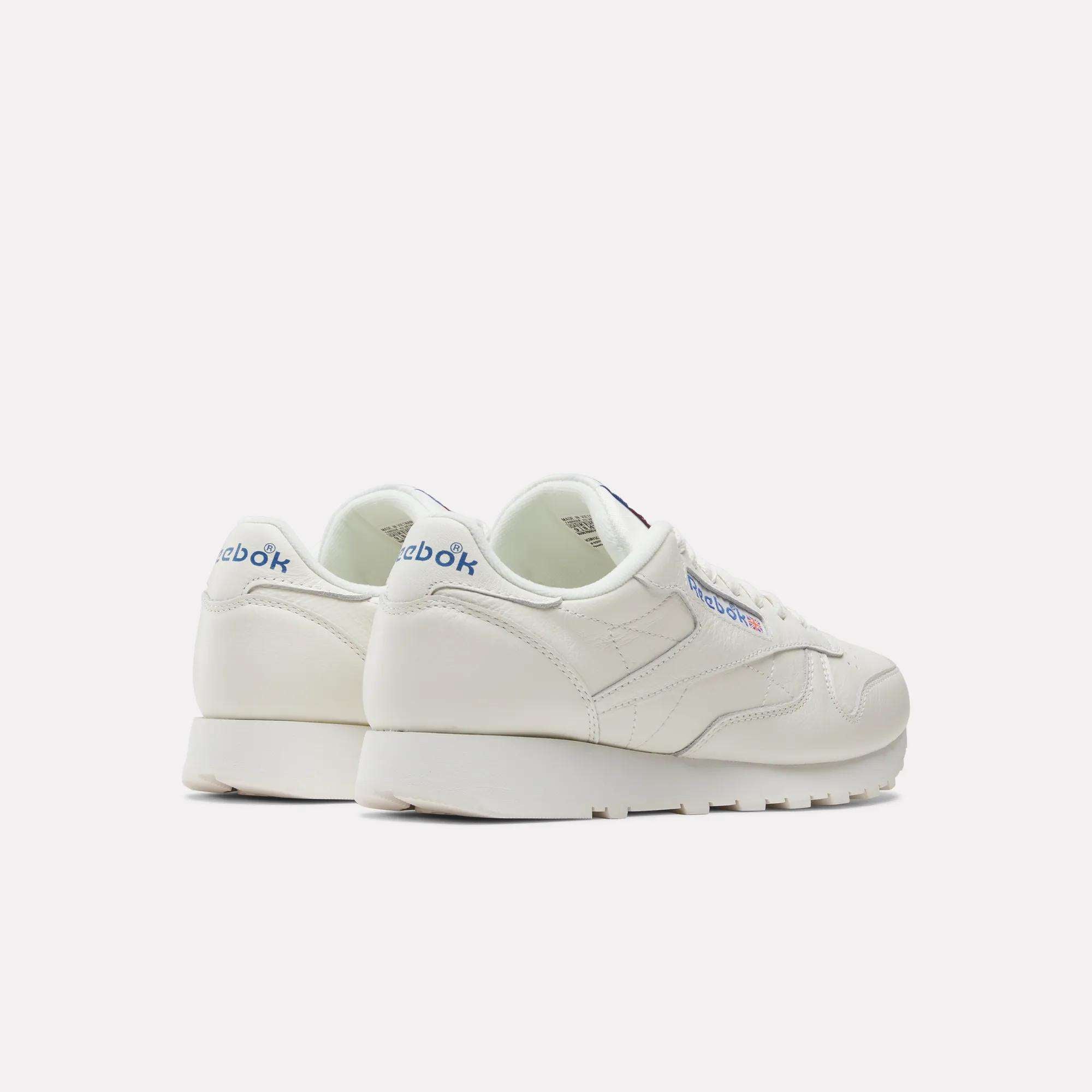 A pair of Reebok Classic Leather Shoes in white, featuring blue Reebok logos on the heel and side, are displayed at an angle to highlight their retro look and durable leather against a plain light background.