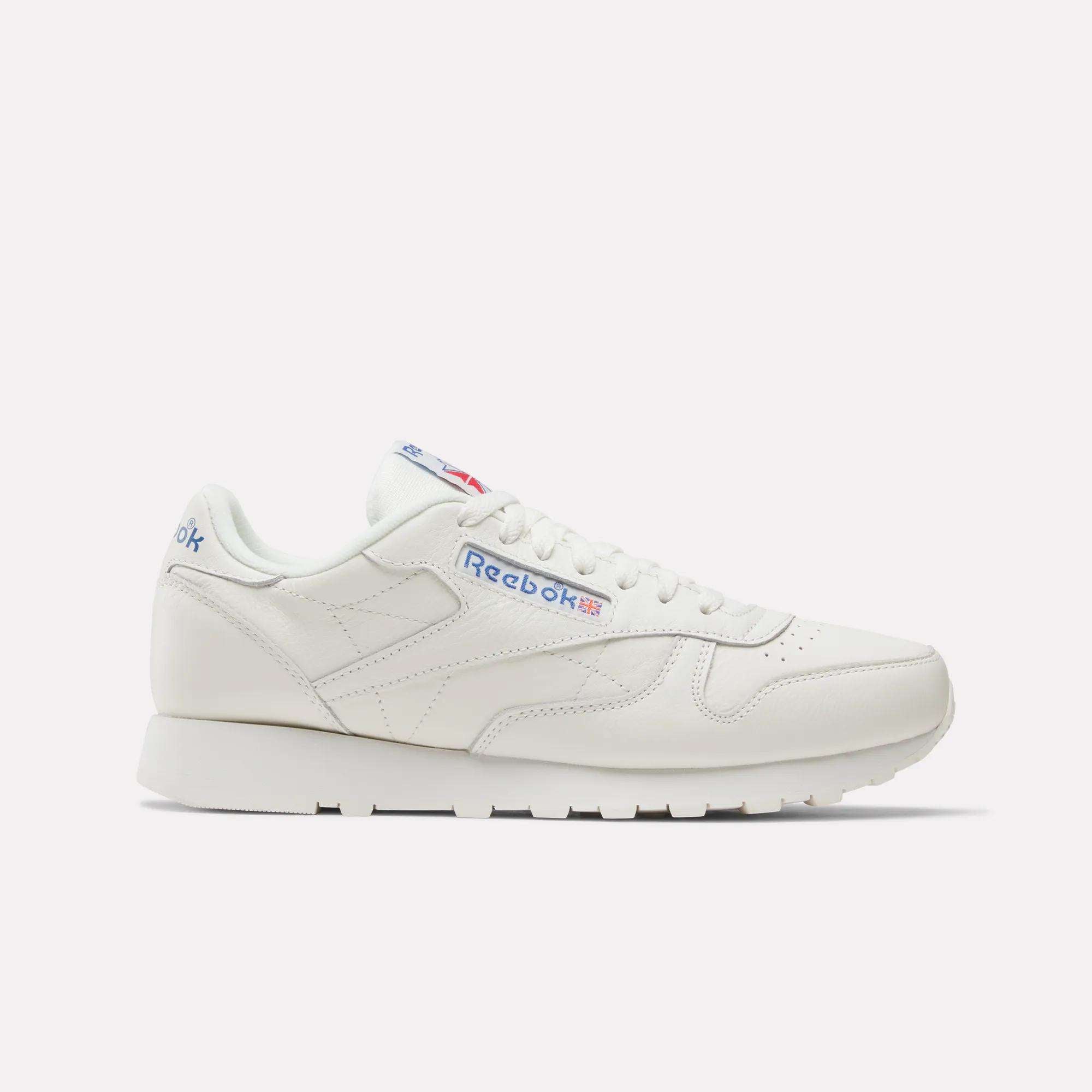 A pair of Reebok Classic Leather Shoes in white with a low profile, crafted from durable leather, featuring blue and red Reebok branding on the side and heel, shown against a plain light background.