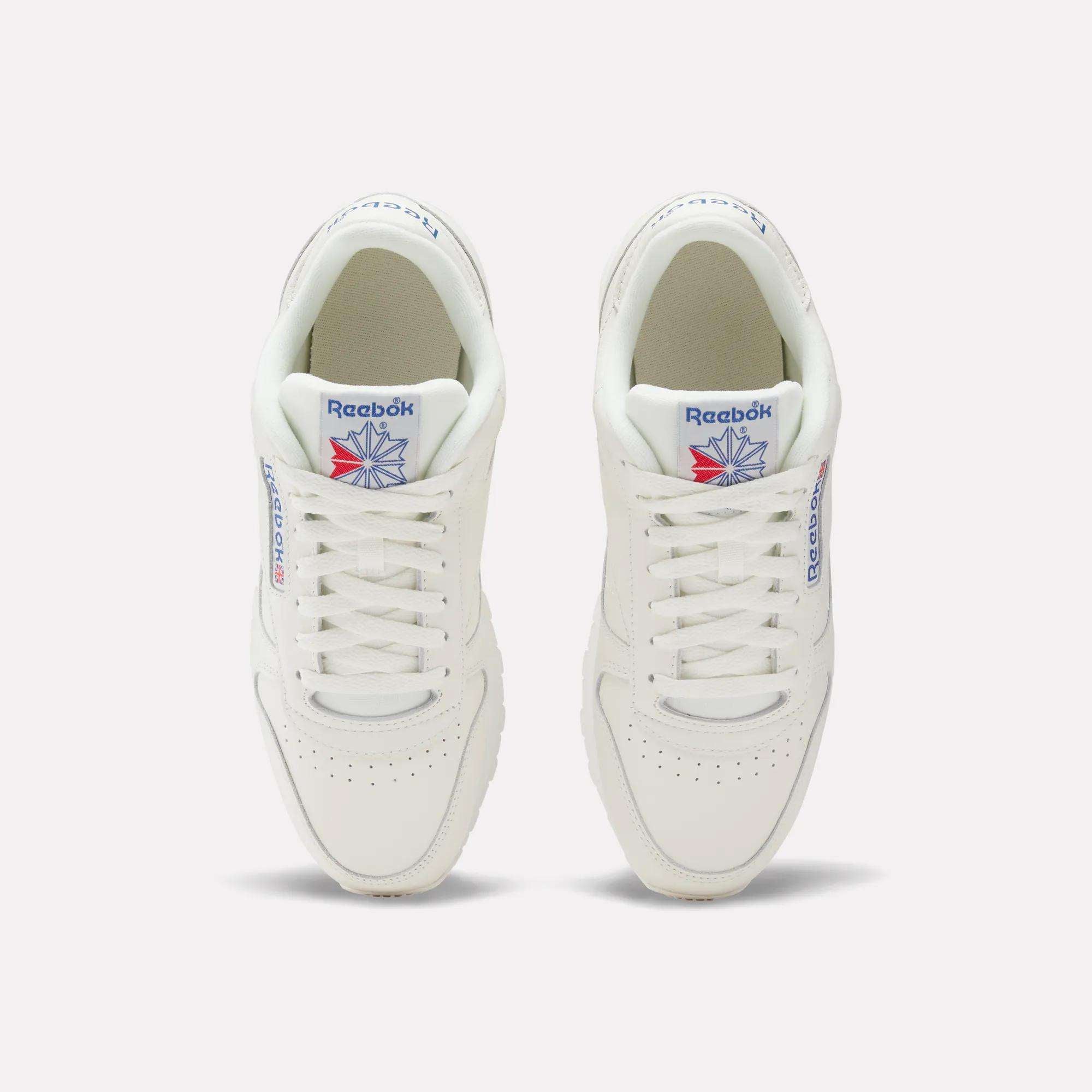 A pair of white Reebok Classic Leather Shoes, seen from above, feature durable leather construction, blue Reebok branding, a red and blue star logo on the tongue, white laces, and perforated detailing on the toes.