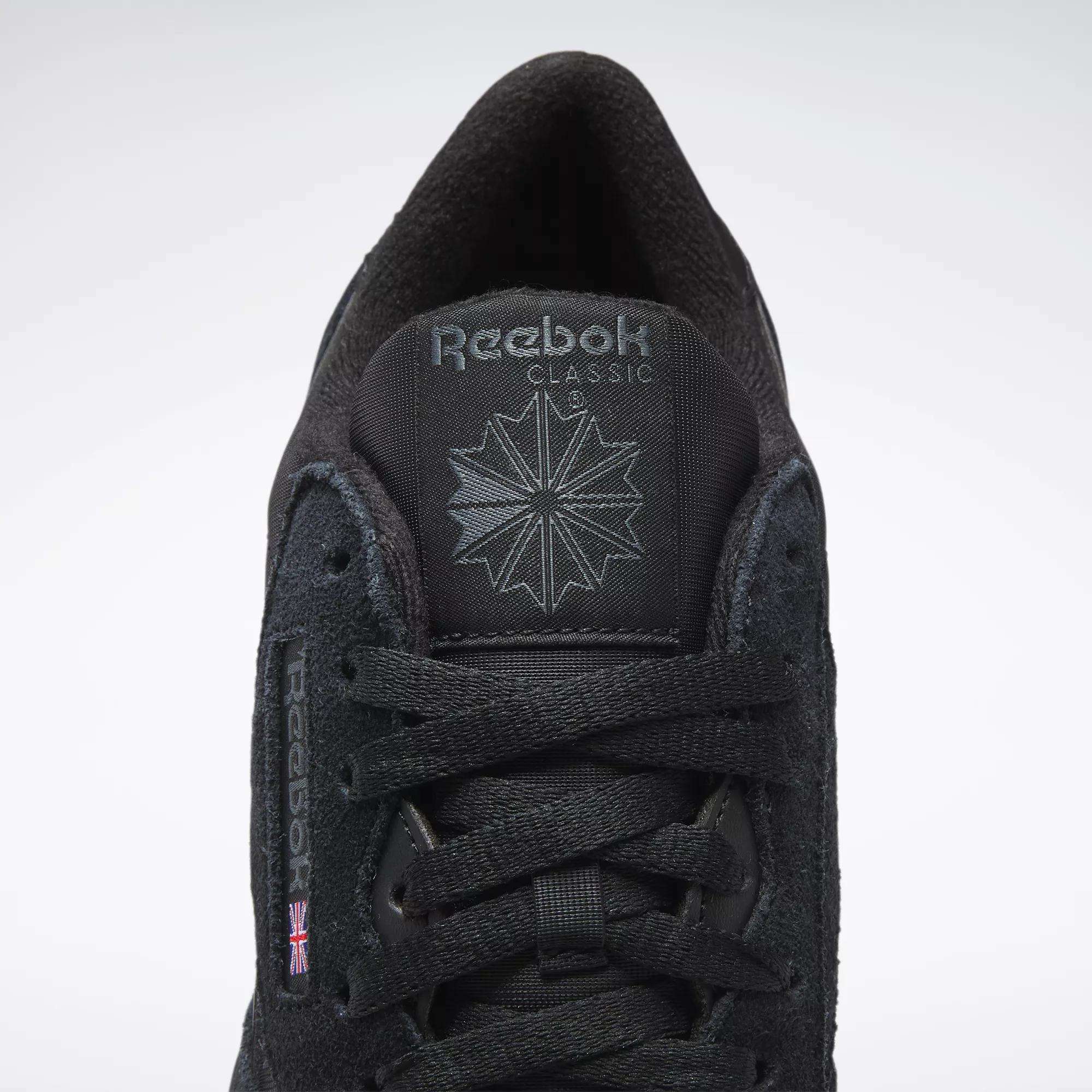 A close-up of Reebok Men's Classic Nylon Shoes features a black nylon upper, black laces, Reebok logo and starburst on the tongue, and a small UK flag on the side—timeless sneakers from Reebok.