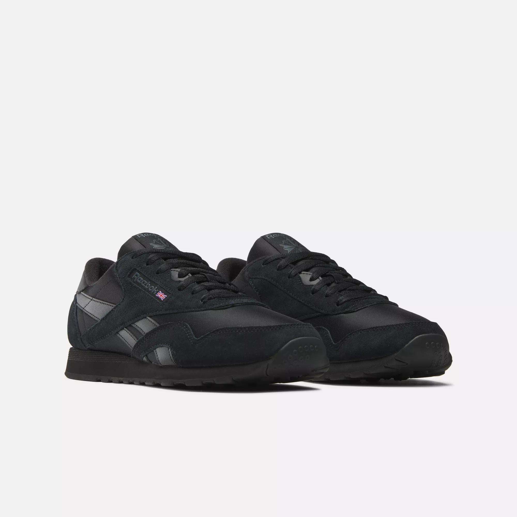 Men's Classic Nylon Shoes by Reebok feature a black nylon upper, black laces and soles, and a small British flag logo on the side. These classic everyday sneakers are shown against a plain white background.
