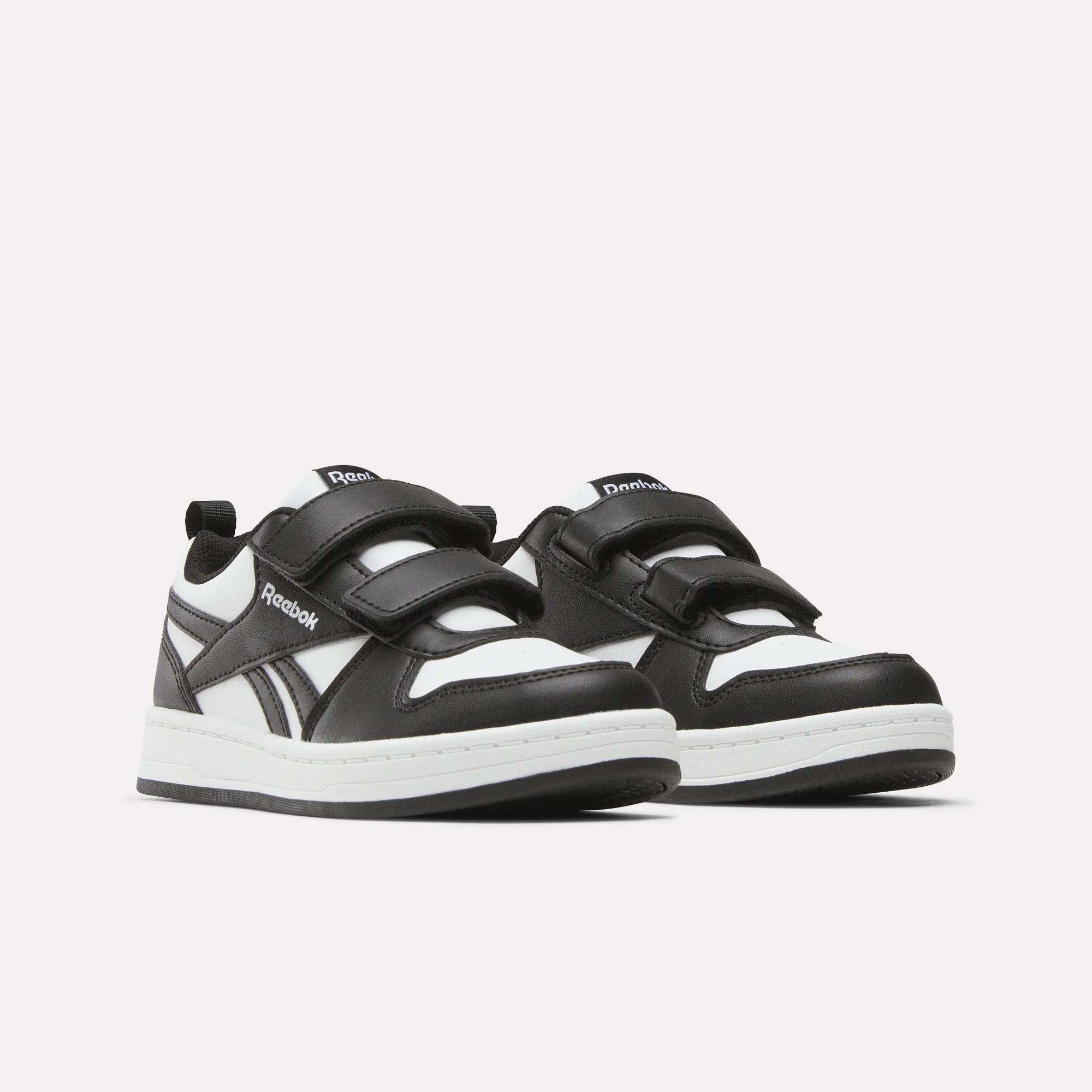 A pair of Kids' Reebok Royal Prime 2 Shoes for little kids, featuring black and white design, two hook-and-loop straps, white soles, and the Reebok logo on the side and tongue, shown against a plain white background.