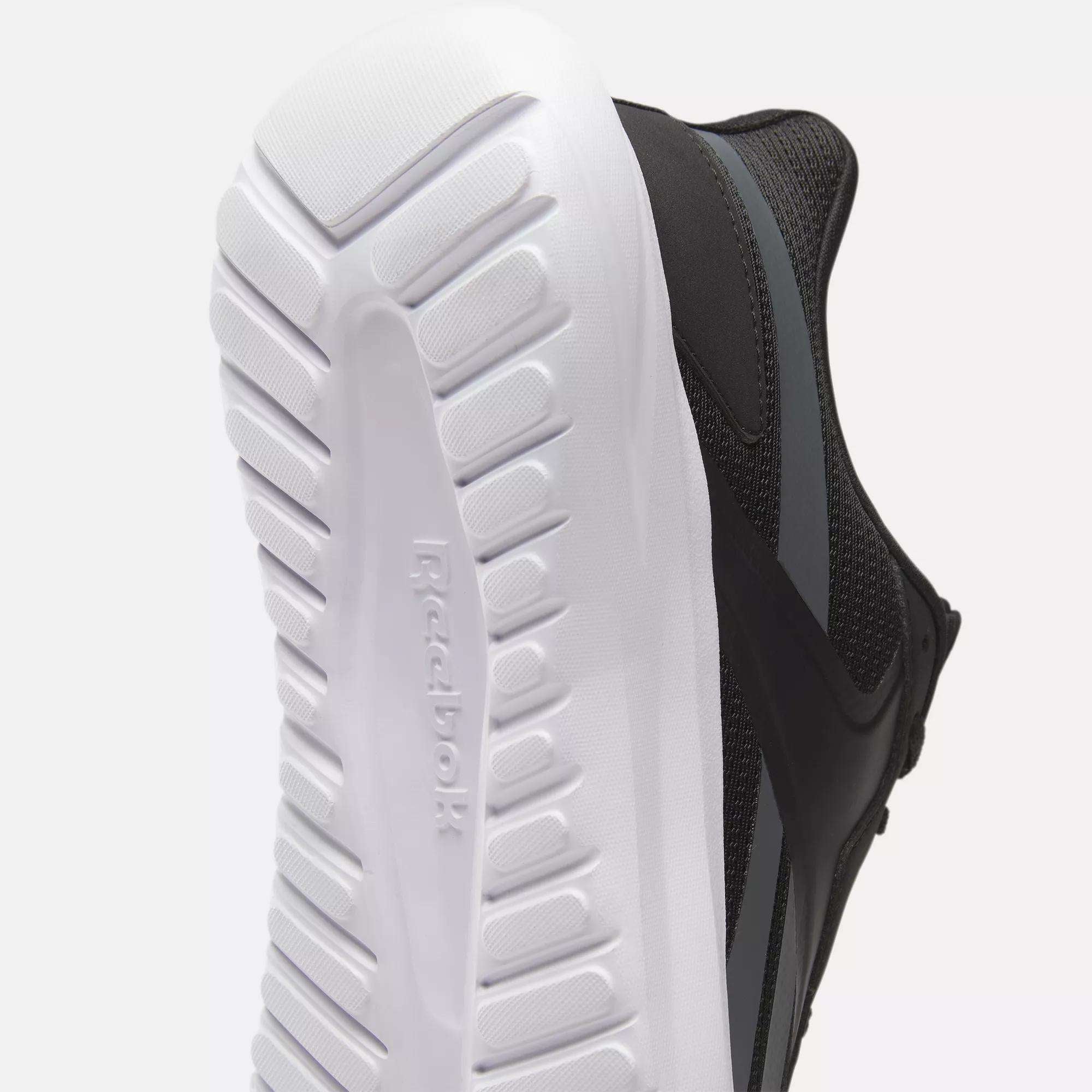 Close-up of the sole and side of a black Reebok Men's Energen Lux Running Shoe, featuring a white textured sole, subtle gray side stripe, and the Reebok logo on the bottom for versatile style.