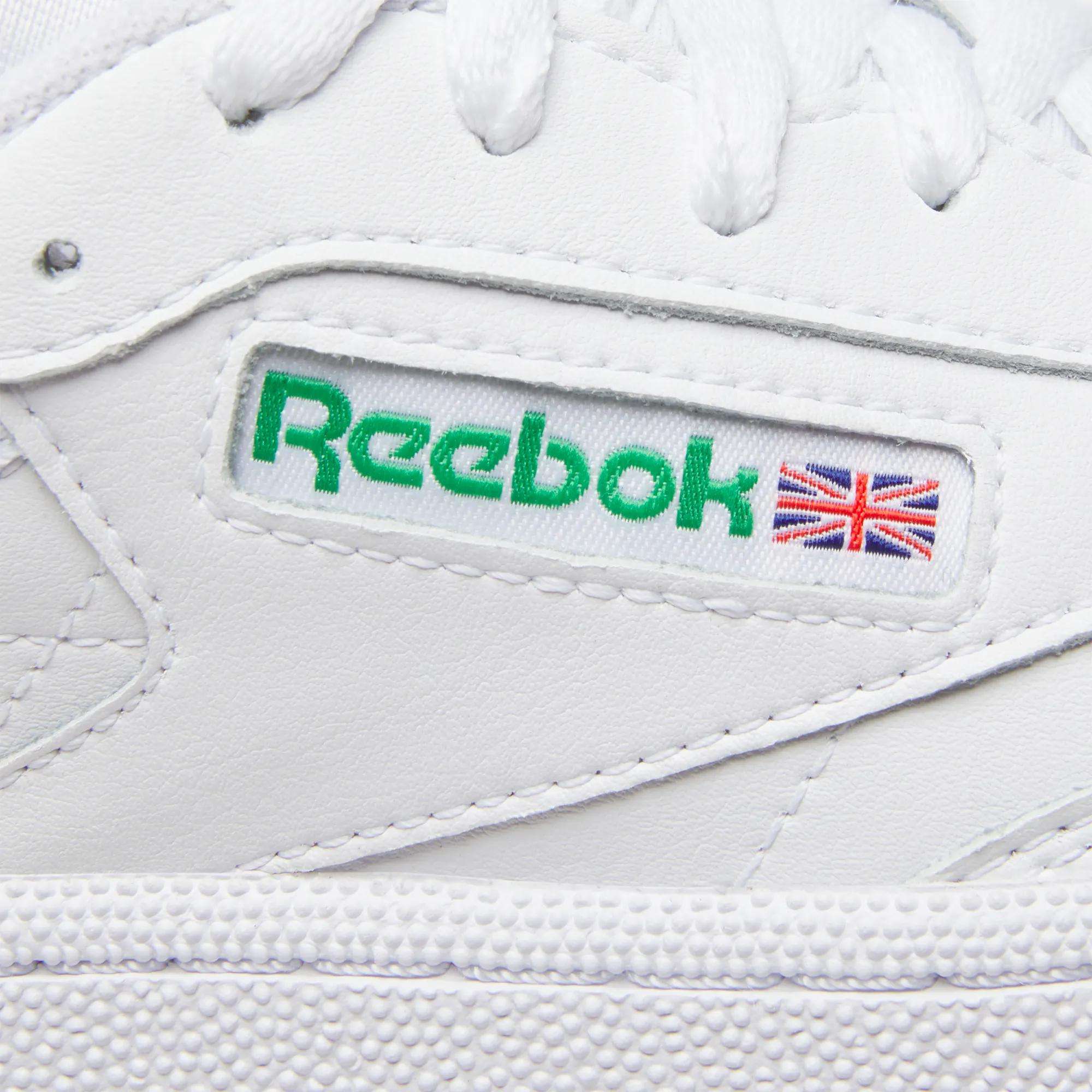 Close-up of Women's Club C 85 Shoes by Reebok, showcasing the green Reebok logo and a small Union Jack flag on a side fabric label—an iconic choice for women’s sneakers.