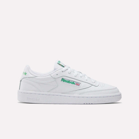 The Reebok Women's Club C 85 Shoes in white with green accents showcase the Reebok logo and a small Union Jack flag on the side, pictured in profile against a plain white background—a stylish choice for women.