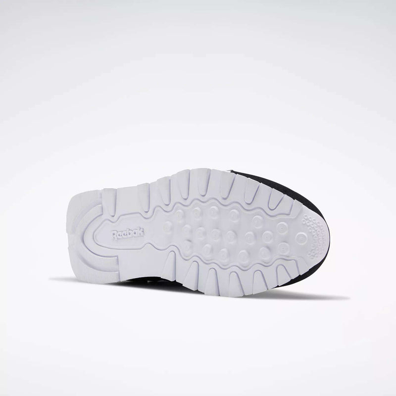 The image displays the sole of Reebok Classic Nylon Shoes - Big Kids facing upward, featuring a white, textured grip pattern and the Reebok logo by the heel. Its minimalist design pays tribute to classic 80s styles against a plain light gray background.