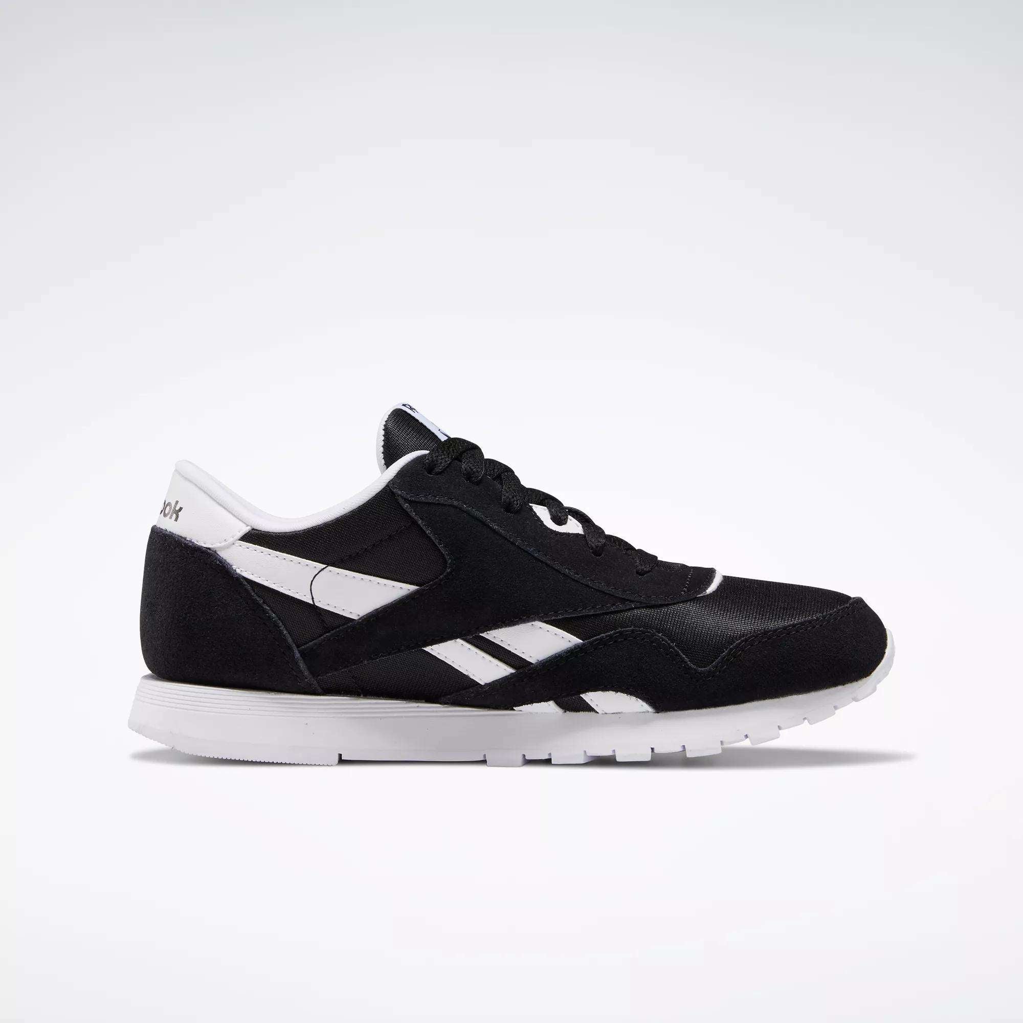 The Reebok Classic Nylon Shoes - Big Kids feature a black and white 80s-inspired minimalist design with side stripes, branding, and a white sole, shown in profile against a light background.